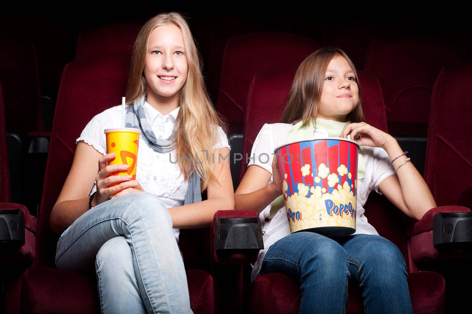 two girls look three-dimensional cinema, sitting in the glasses, eat popcorn, drink drink