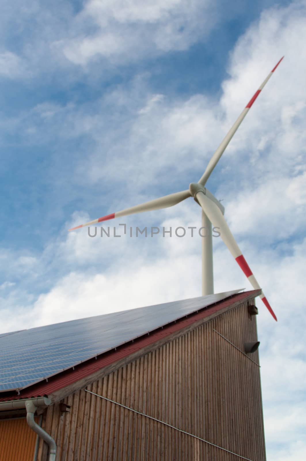 barn covered with solar panels and wind turbine in the background