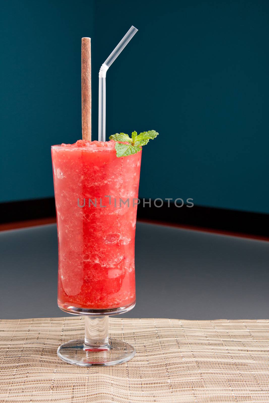 Red fruit flavored frozen cocktail or smoothie beverage with straw and stirring stick.