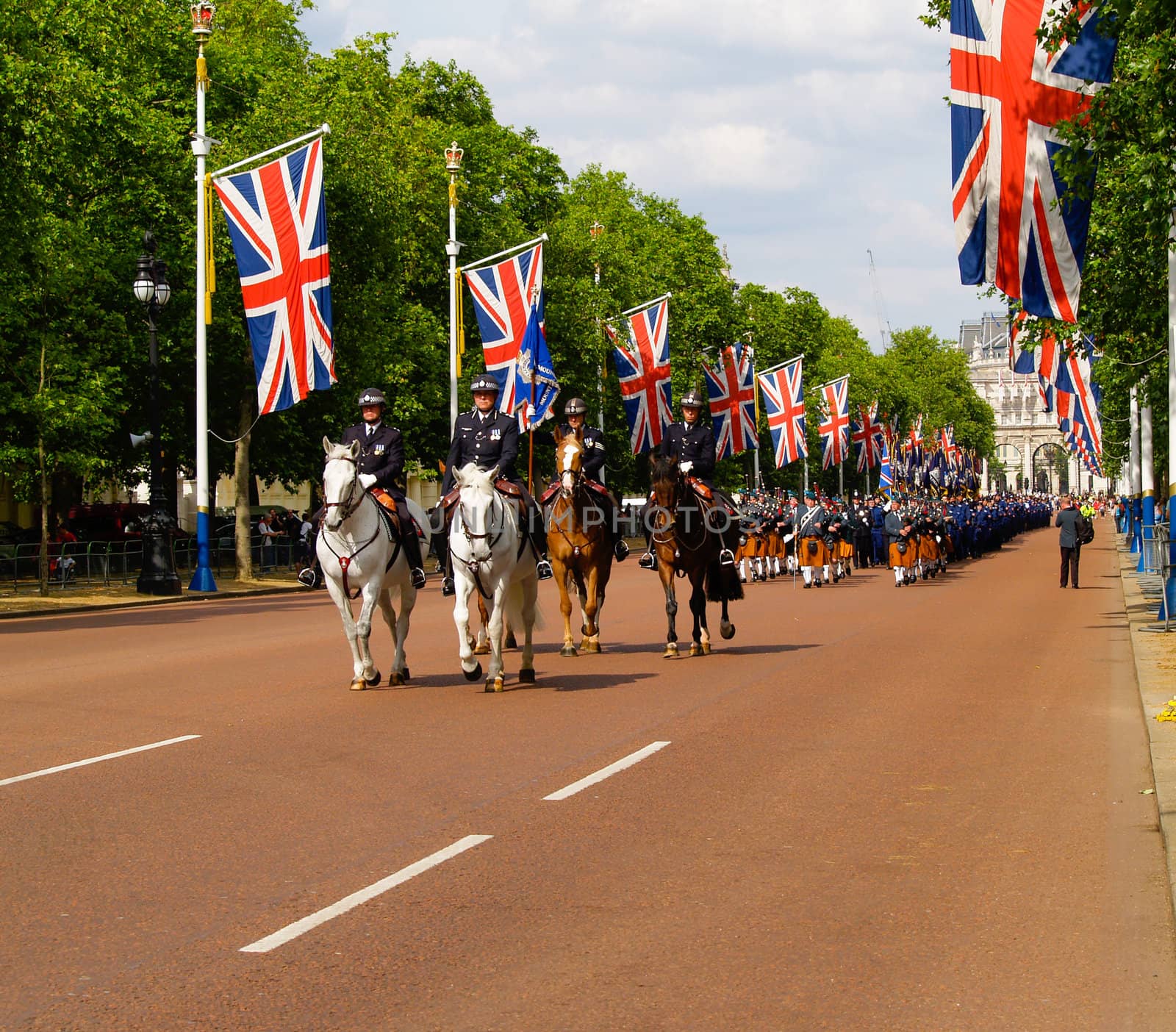 Band of marching bagpipers are lead along London's Mall by mounted flag bearers.