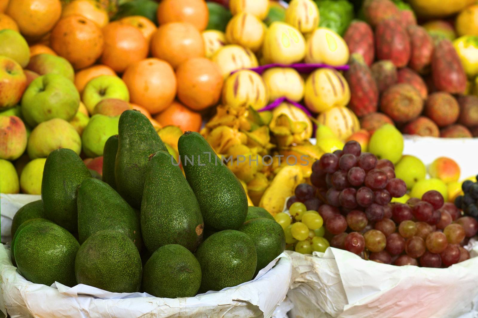 Avocado and other fruits such as grapes, apples, star fruits and oranges in piles on a Peruvian market (Selective Focus, Focus on the avocados)