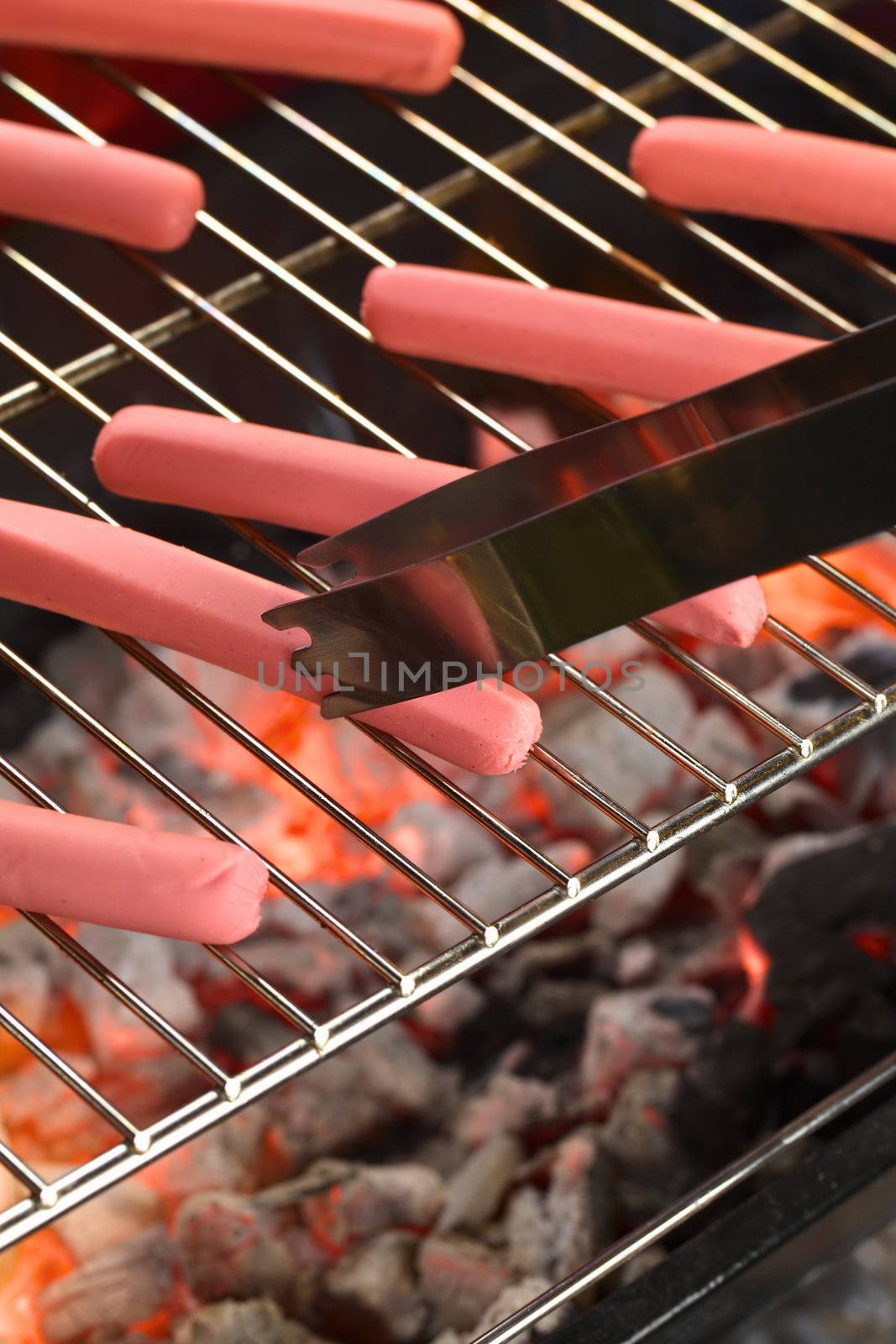 Sausages on barbecue with tongs with glowing charcoal below (Selective Focus, Focus on the end of the tongs and the lower end of the sausage they touch)