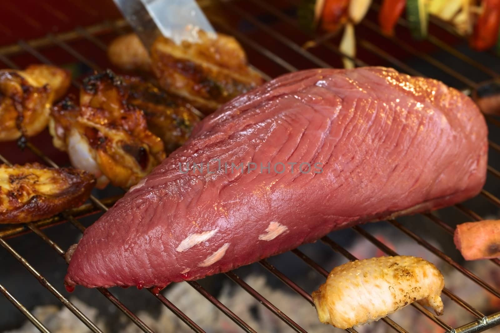 Big piece of beef meat with chicken wings and vegetable skewers on barbecue (Selective Focus, Focus on the left end of the beef meat) 