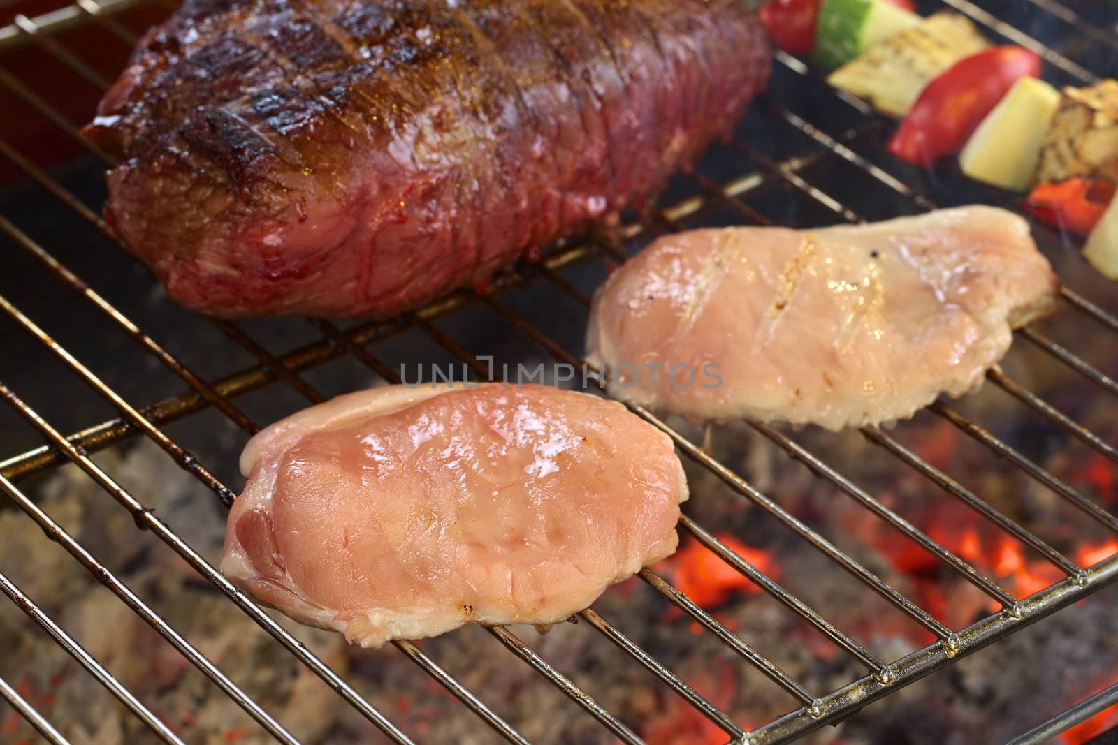 Two slices of pork meat with beef meat and vegetable skewers on barbecue with glowing charcoal below (Selective Focus, Focus on the front of the first pork meat slice)