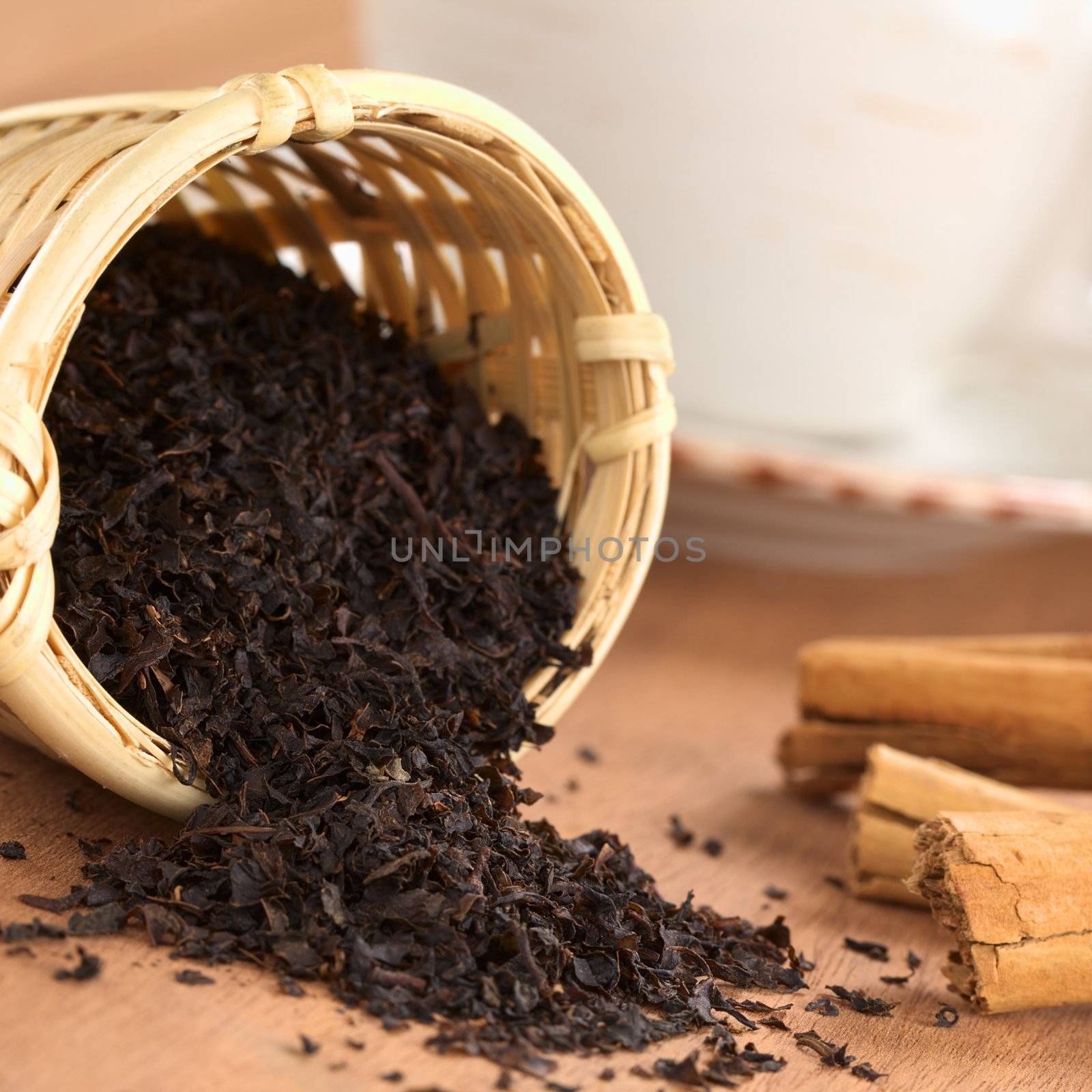 Loose black tea in wooden tea infuser with cinnamon sticks and tea cup (Selective Focus, Focus on the tea leaves at the rim of the infuser) 
