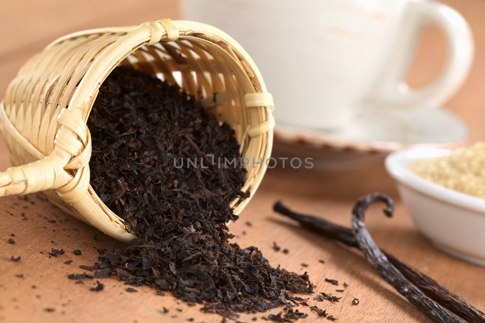 Loose black tea in wooden tea infuser with vanilla sticks, brown sugar and tea cup (Selective Focus, Focus on the tea leaves at the rim of the infuser) 