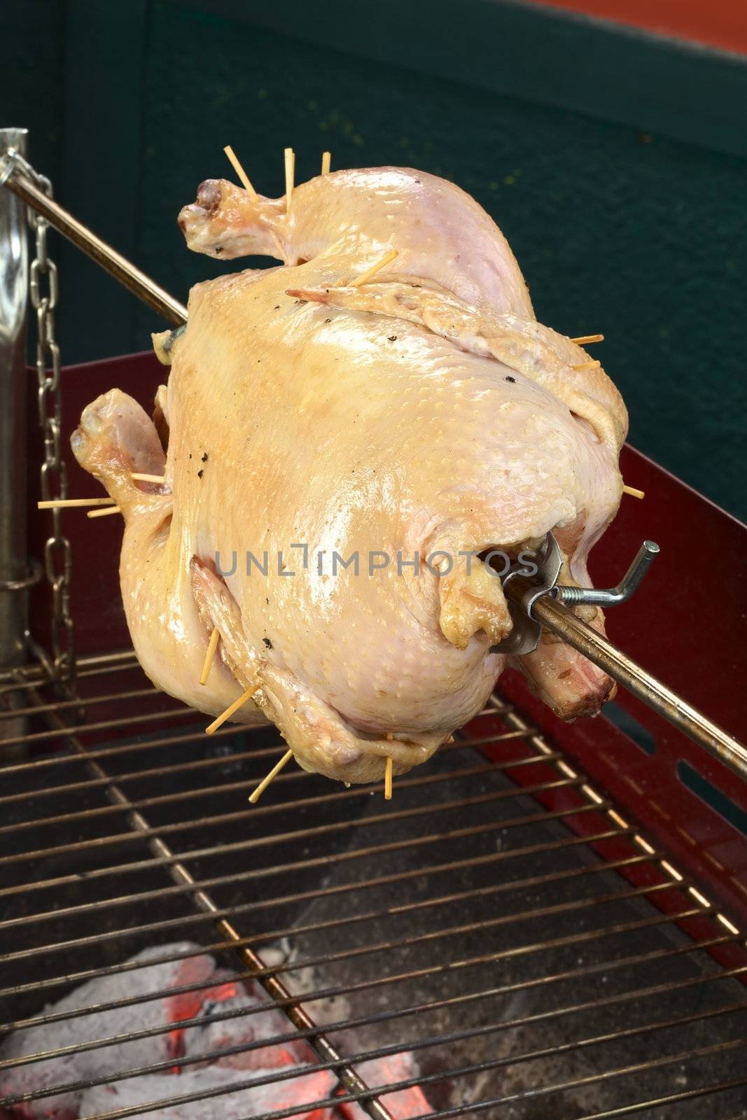 Whole chicken being grilled on spit over a charcoal barbecue (Selective Focus, Focus on the front of the chicken)