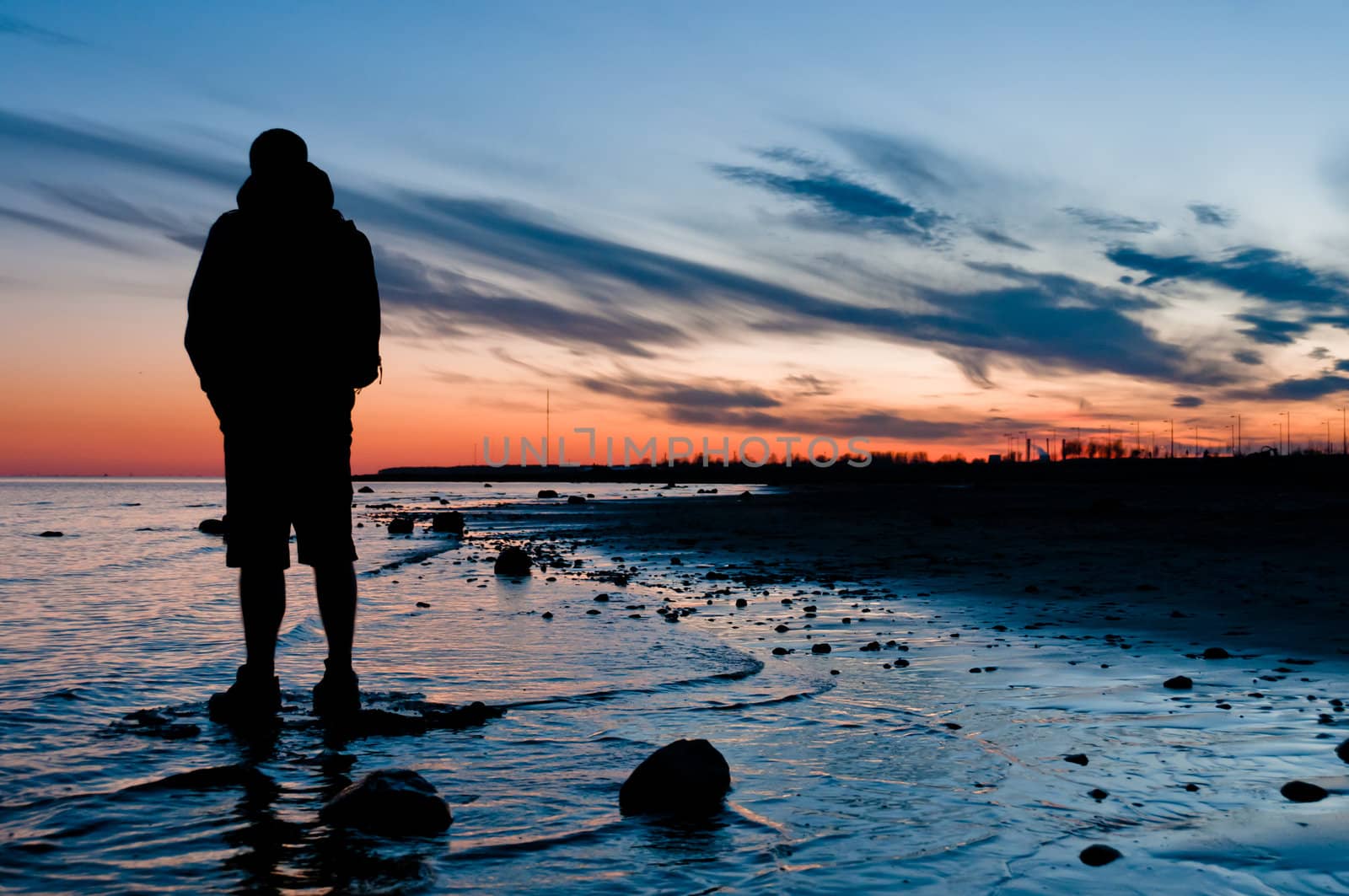 Traveler looking on sunset, standing in water near beach
