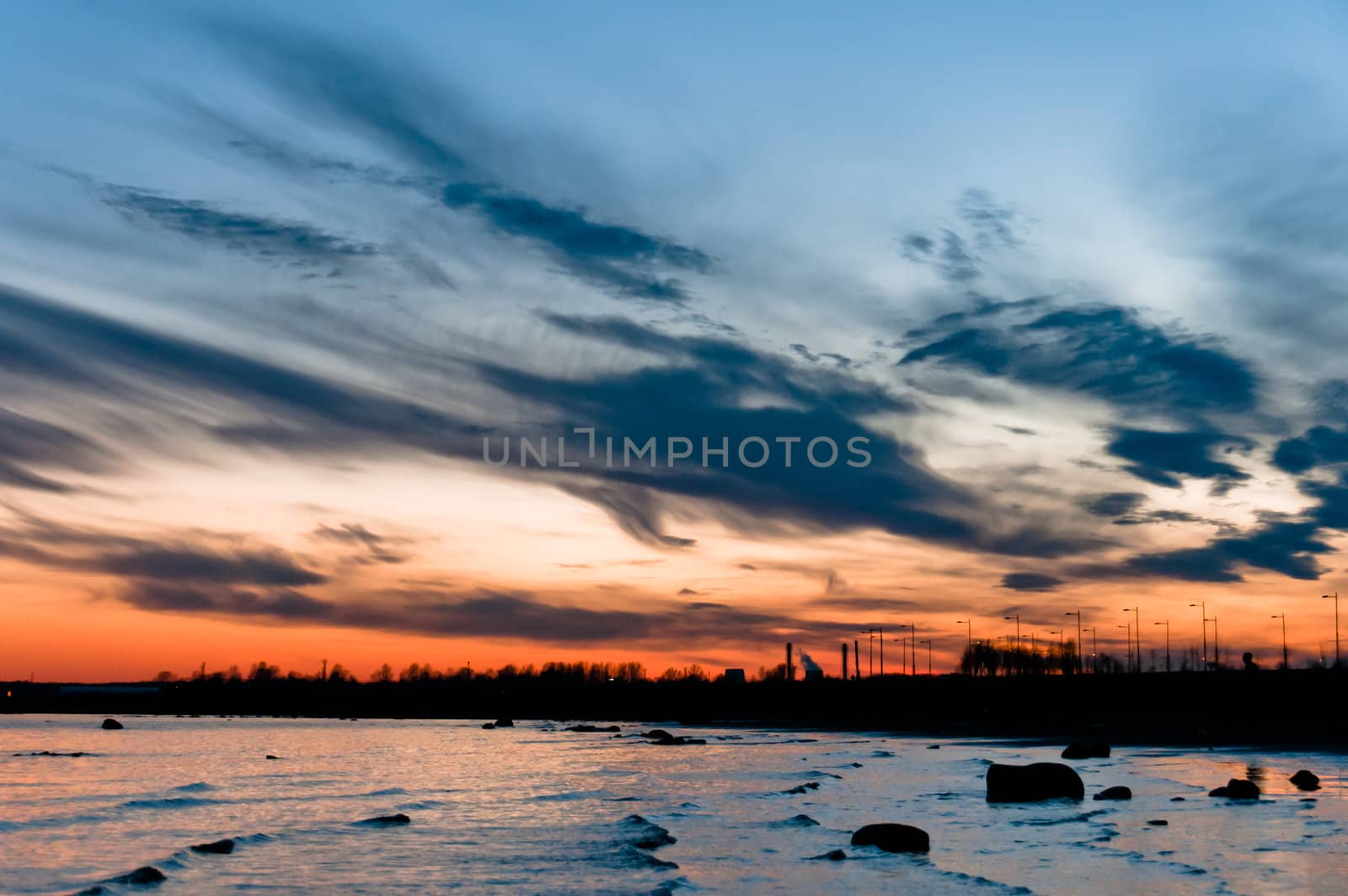 Late sunset over the lake with beautiful cloudscape and stones silhouettes