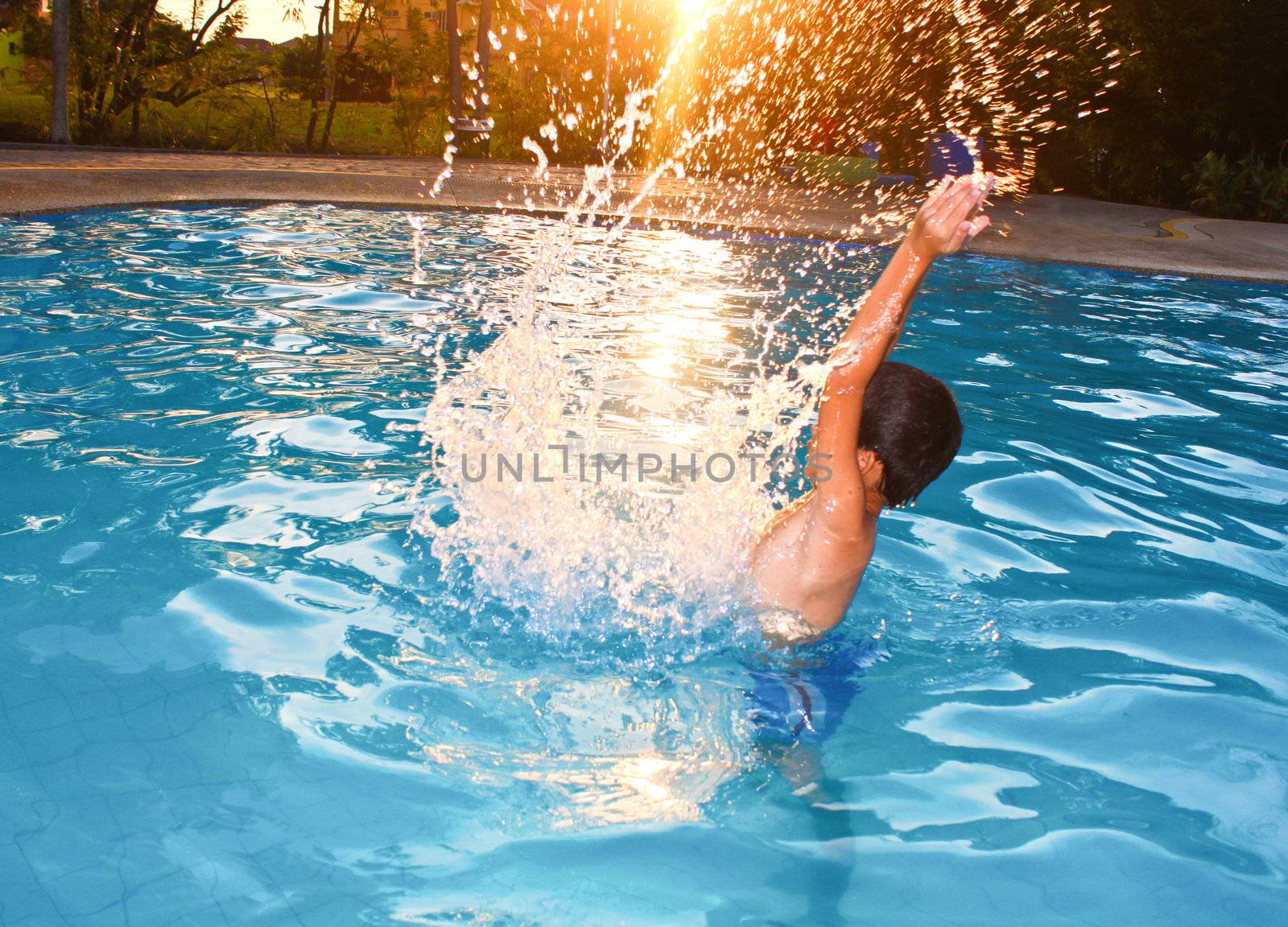 Asian young boy splashing in water as the sun glowing it's light.