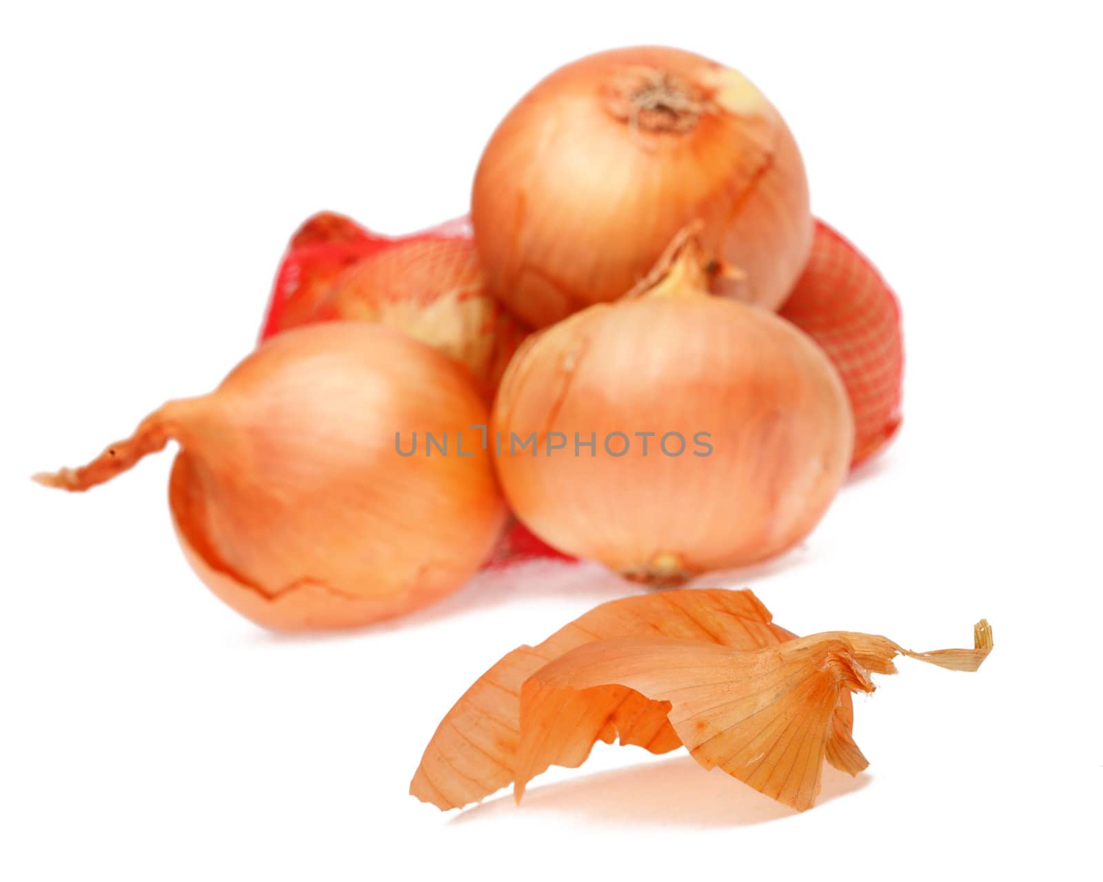 A piece of a thin onion peel in fornt of a heap of onions against a white background.Selective focus on the peel.