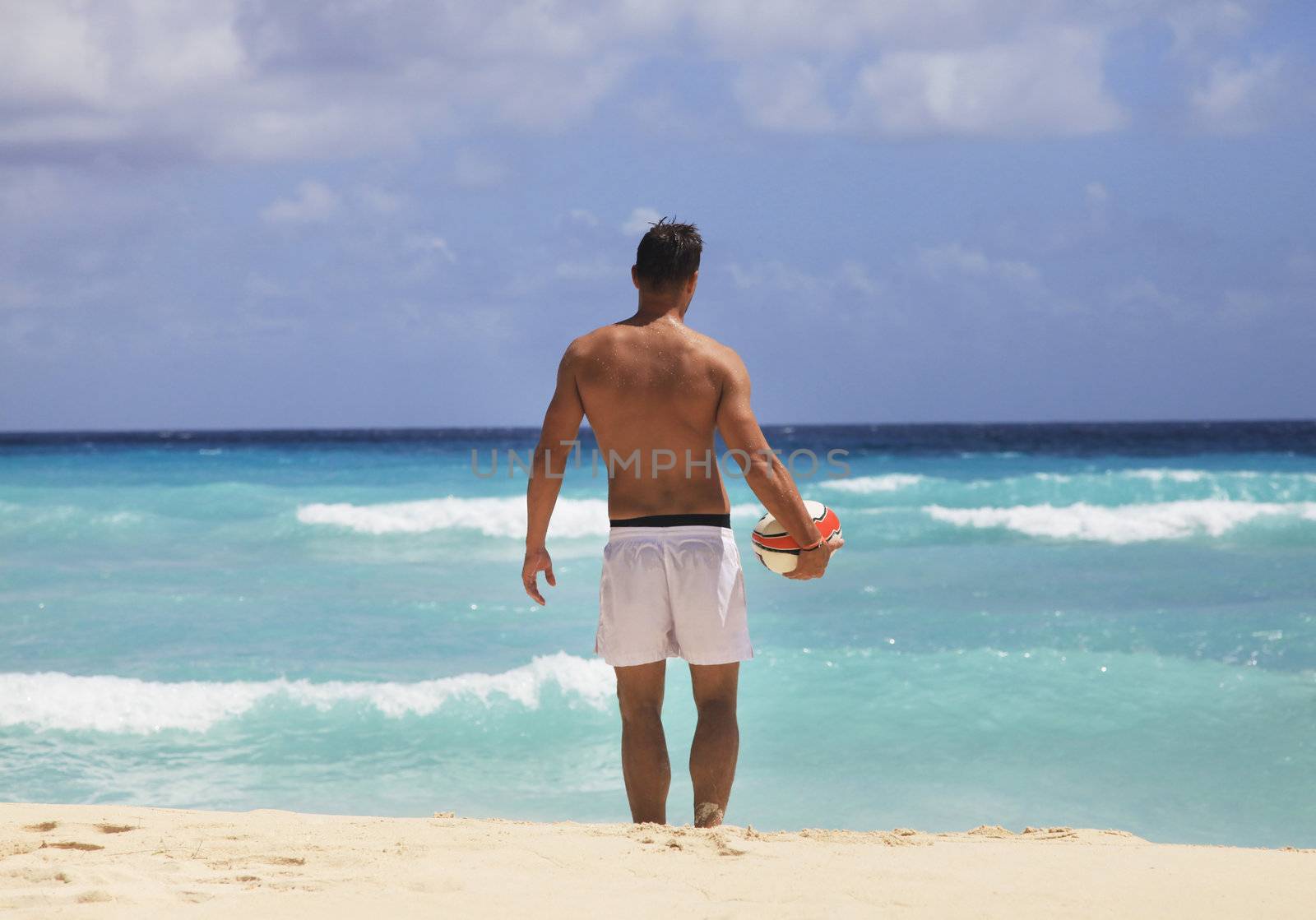 Young man with ball on beach.