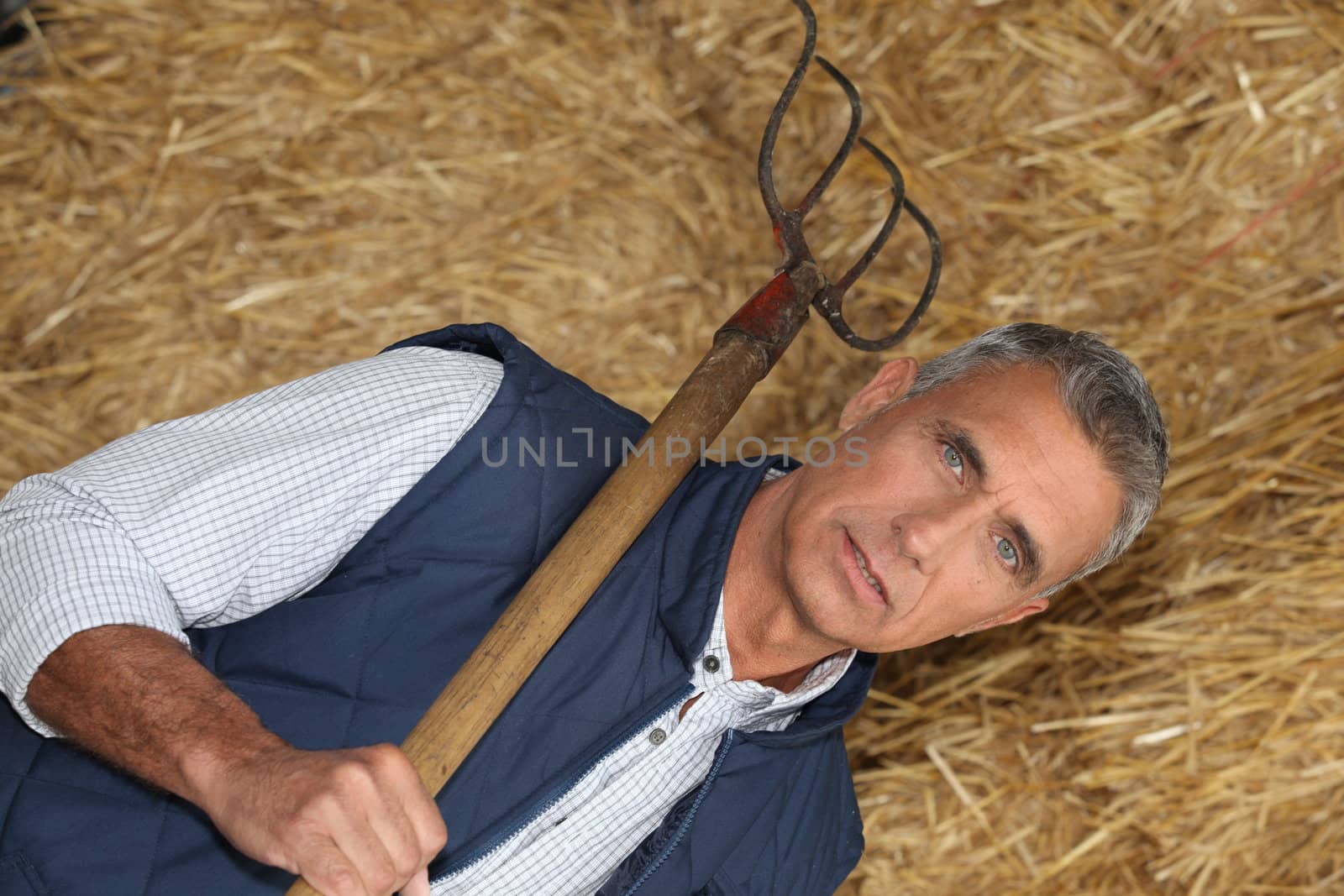 mature handsome farmer posing with fork against hay background