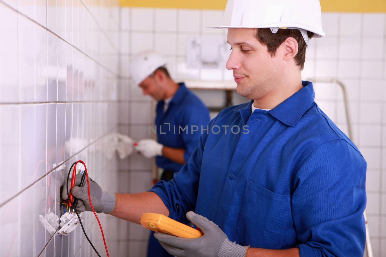 Two young electricians at work in a tiled room