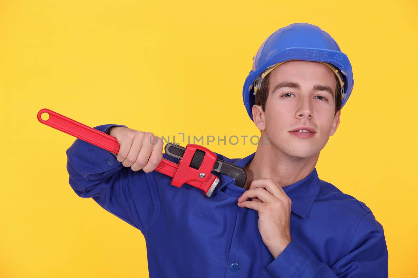 portrait of young plumber holding adjustable spanner against yellow background