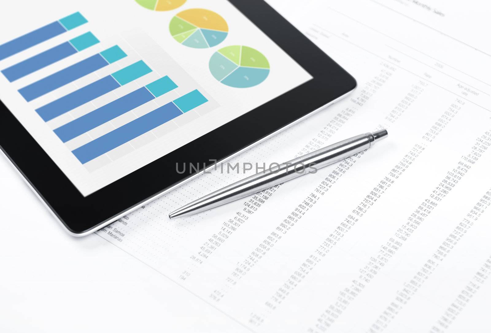 Modern workplace with digital tablet showing charts and diagram on screen, pen and paper with numbers.