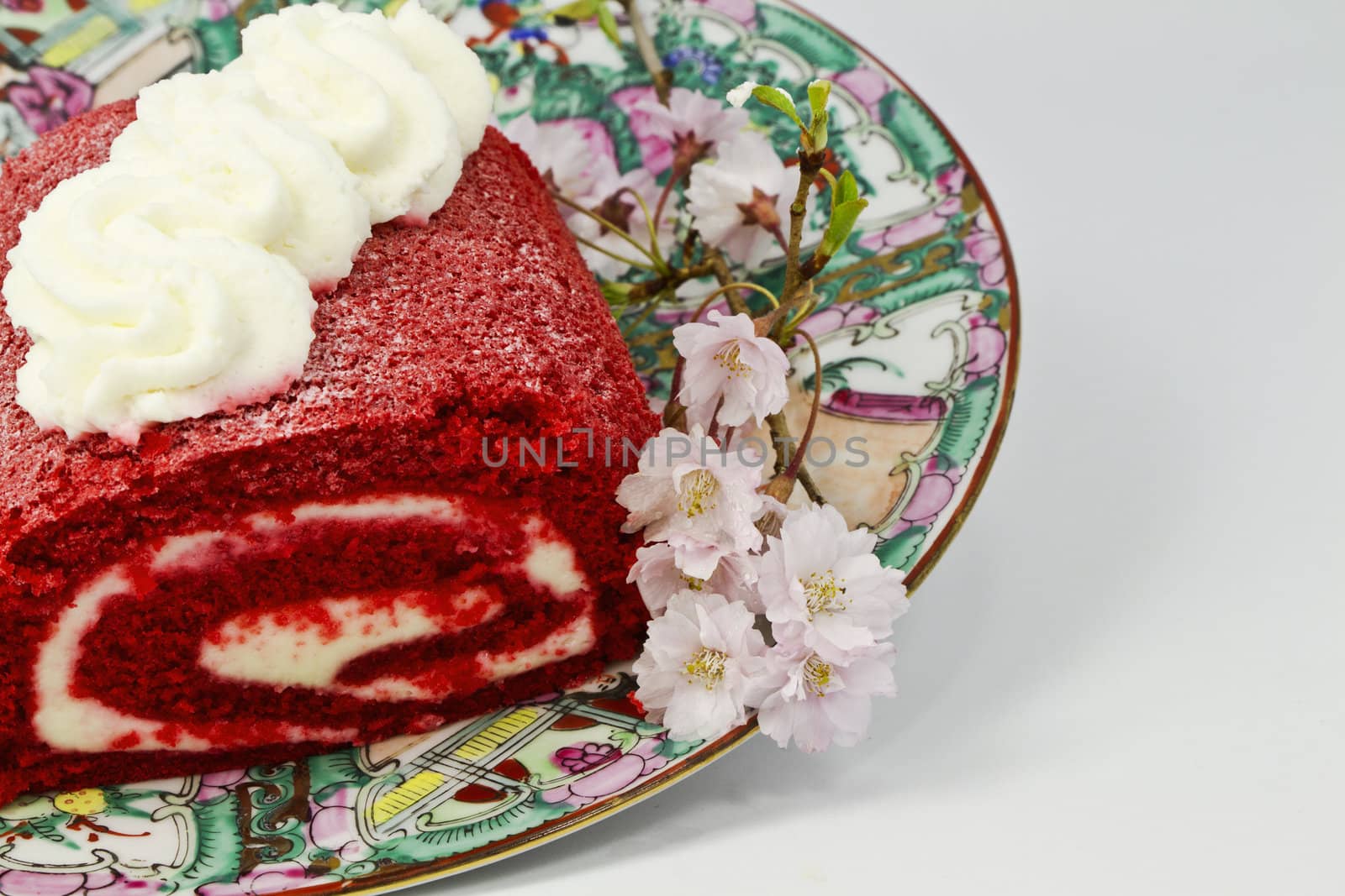 Red velvet cake roll with cream cheese frosting,  inside and on top, is placed on feminine platter with pink flowers; 