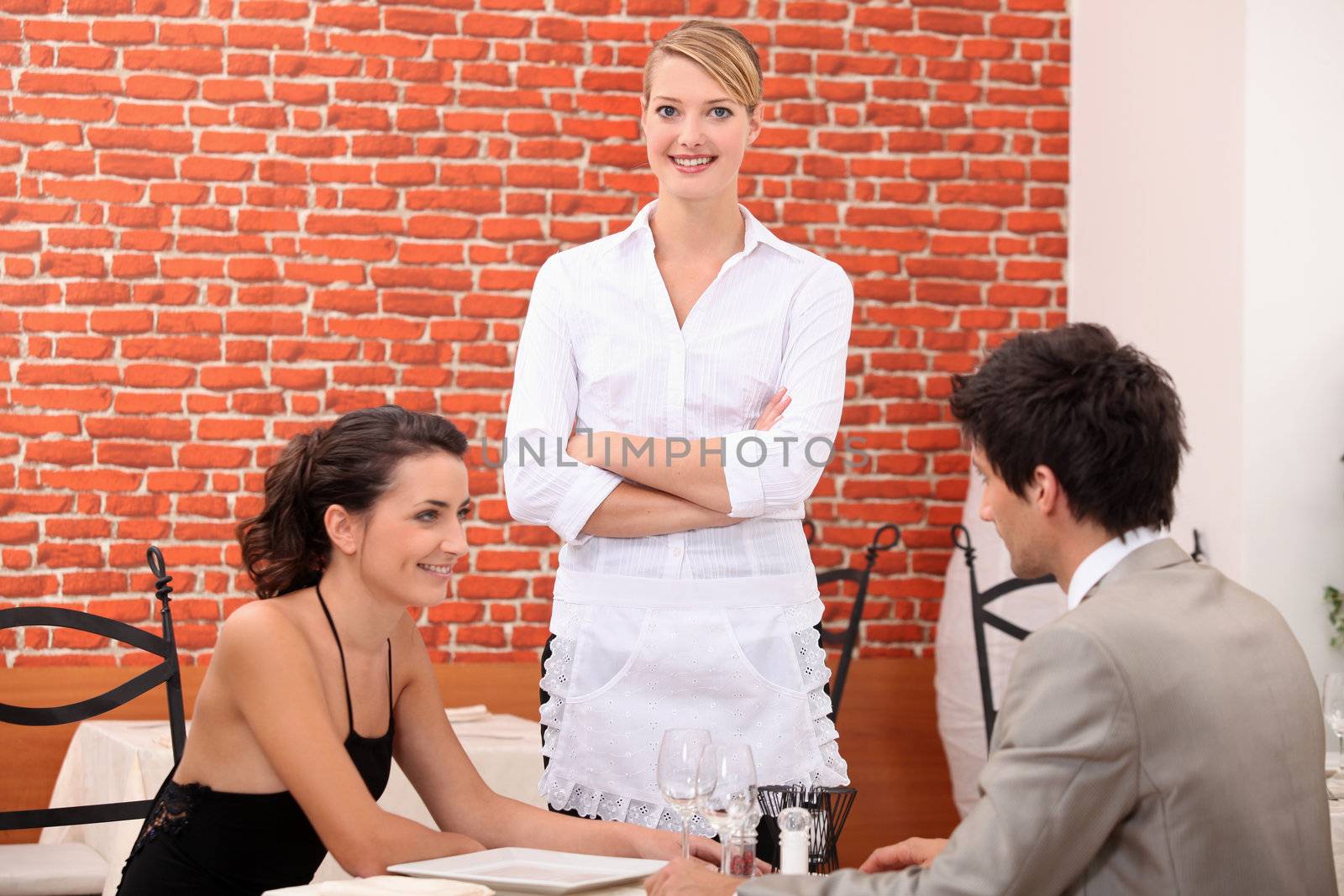 a couple dining at a restaurant and a waitress crossing her arms by phovoir