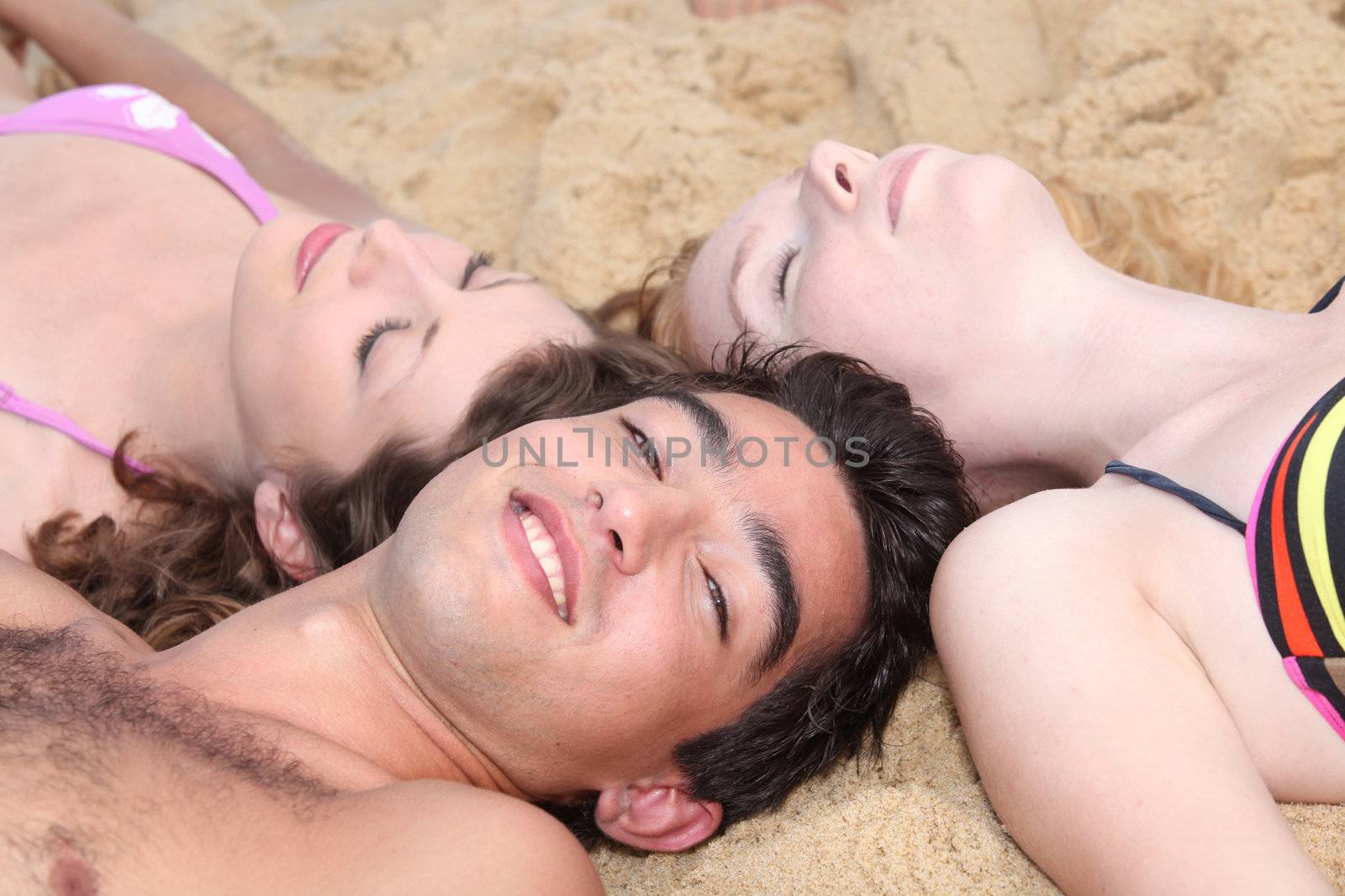 Three young people lying in the sand by phovoir