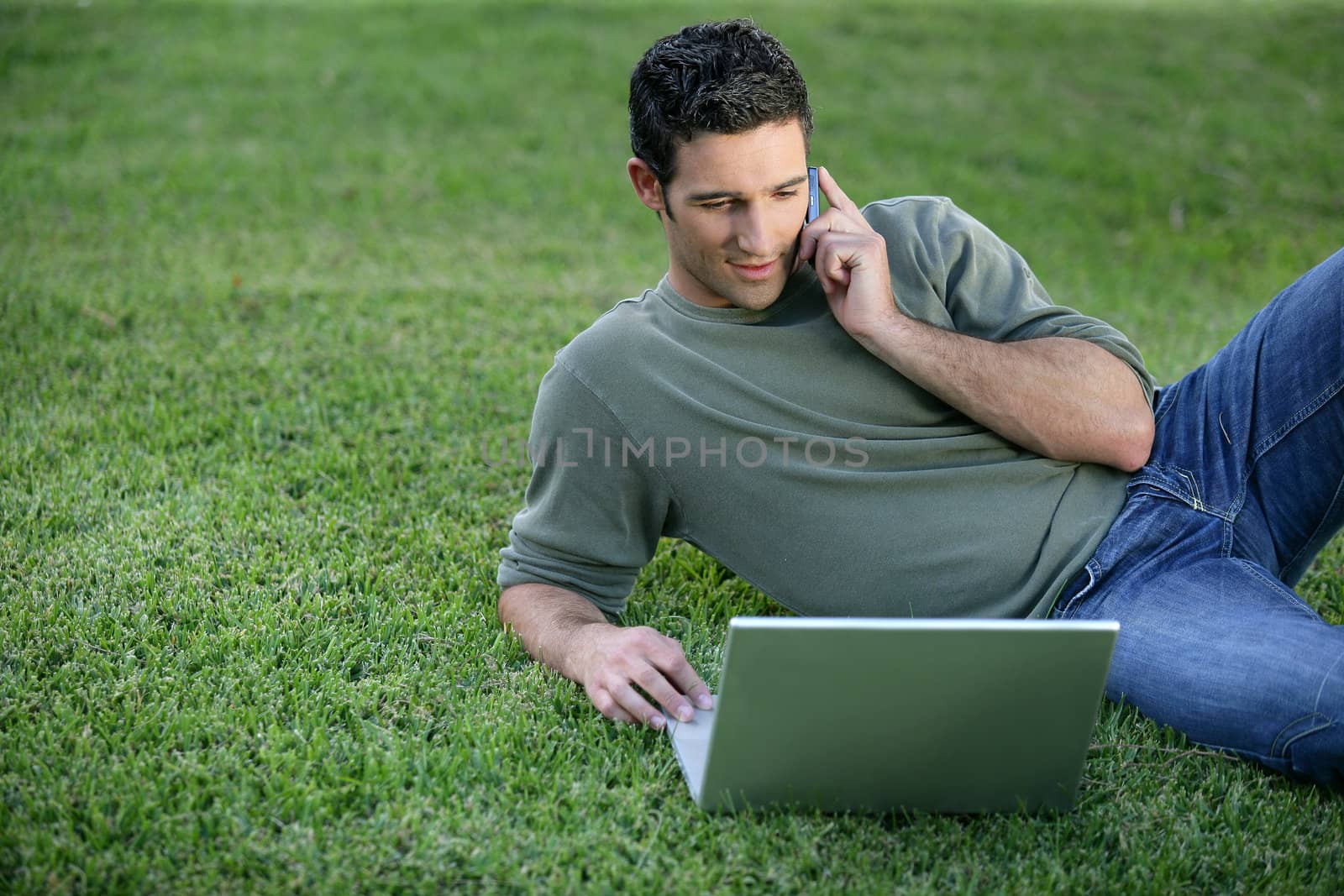 Relaxed man using phone and computer laid on the grass