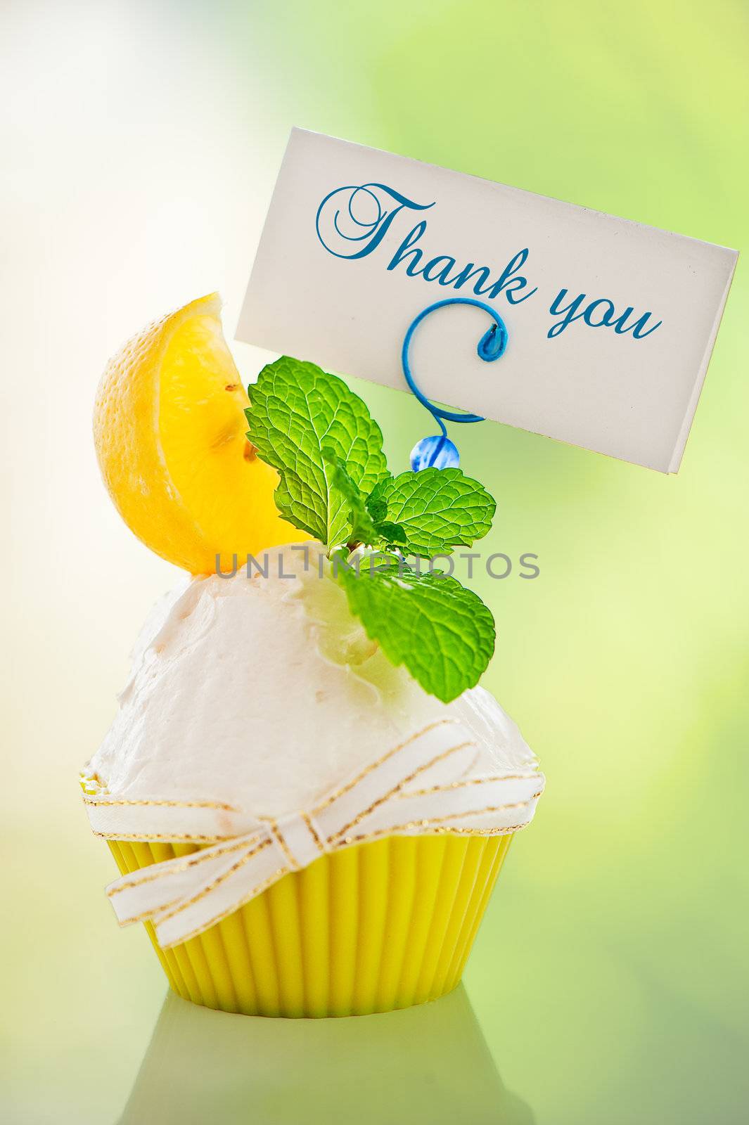 A refreshing lemon cupcake with a leaf of mint and a label for your text on green background as a studio shot