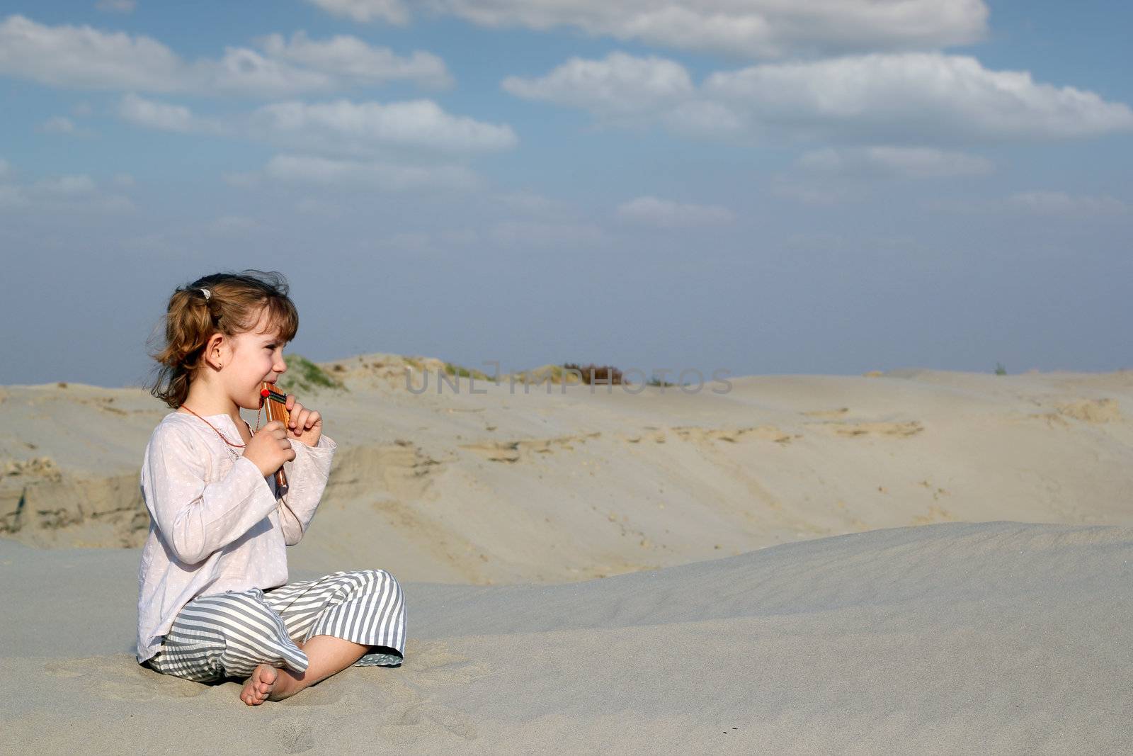 little girl sitting on sand and play music