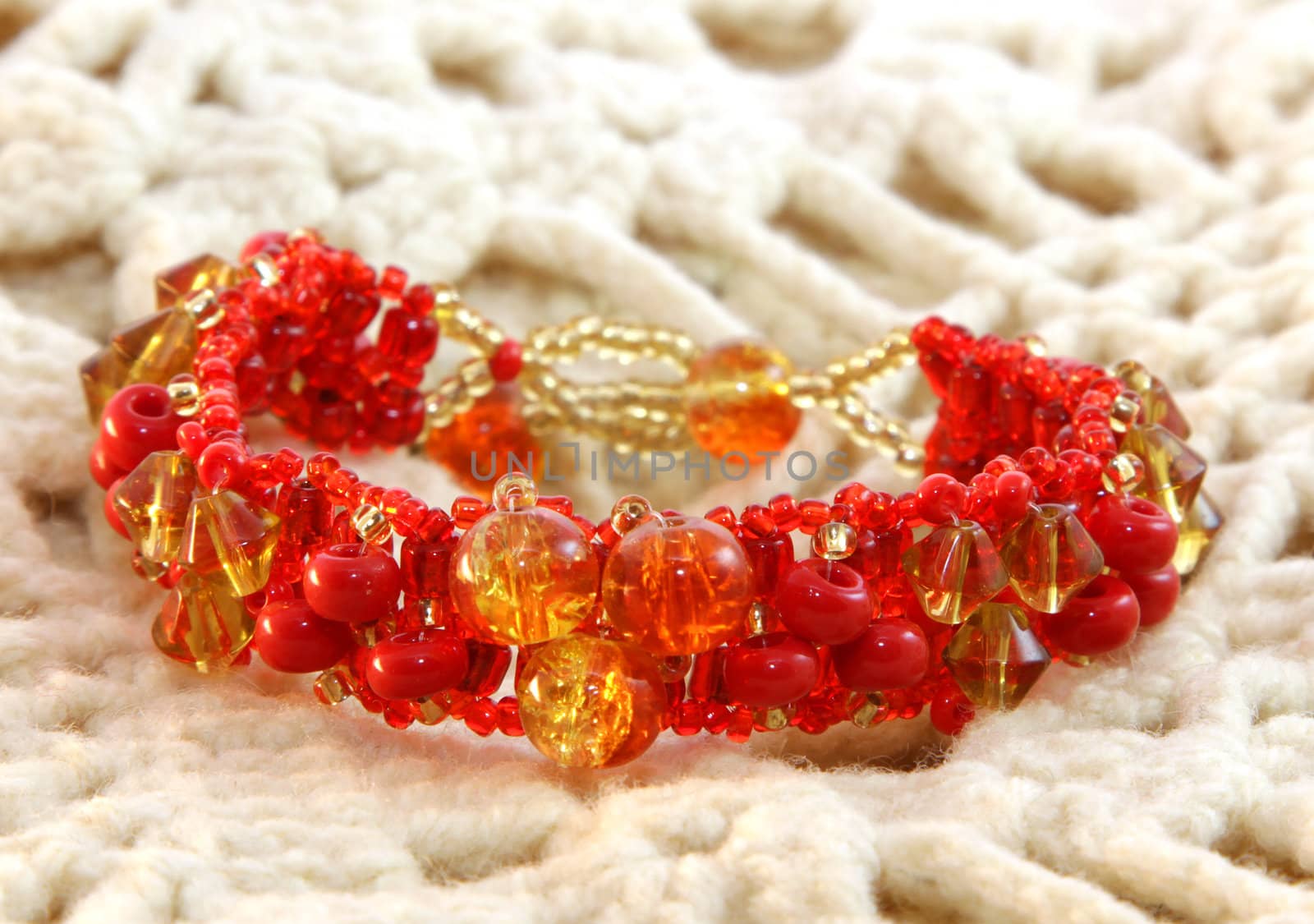 Red bracelet handmade from glass on a knitted background
