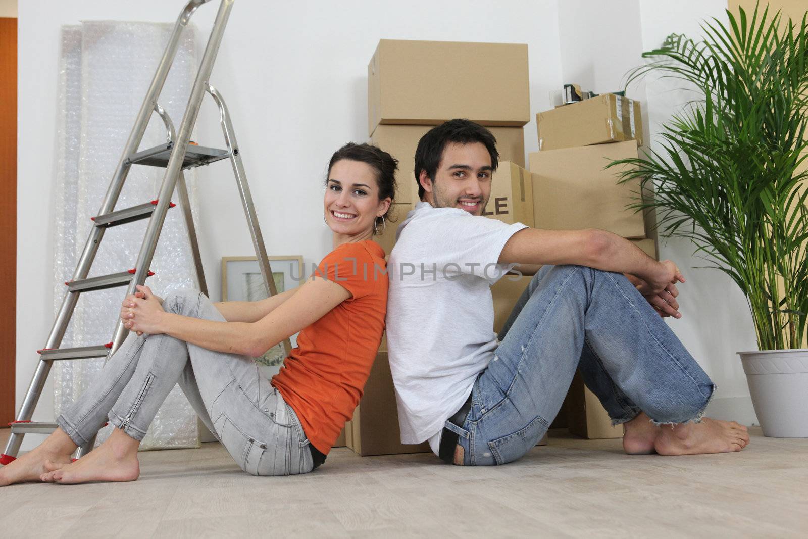 Couple sitting back to back next to step ladder