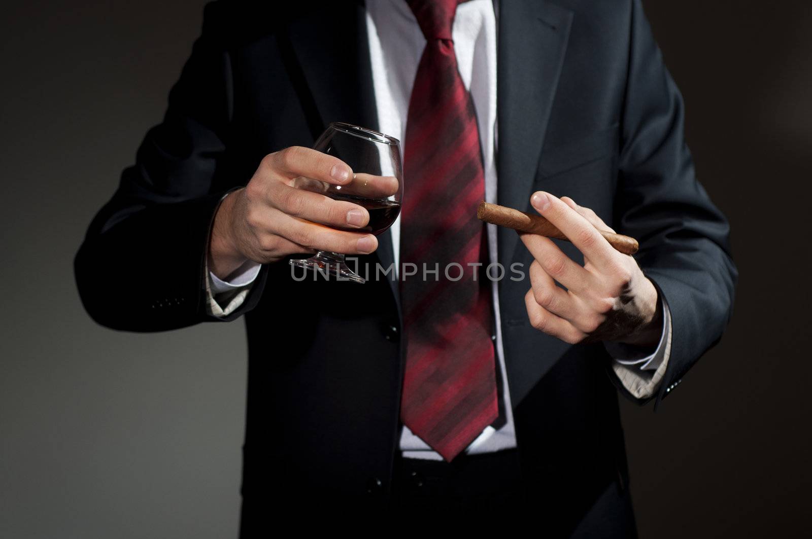 man in a business suit holds a cigar and a glass with whisky