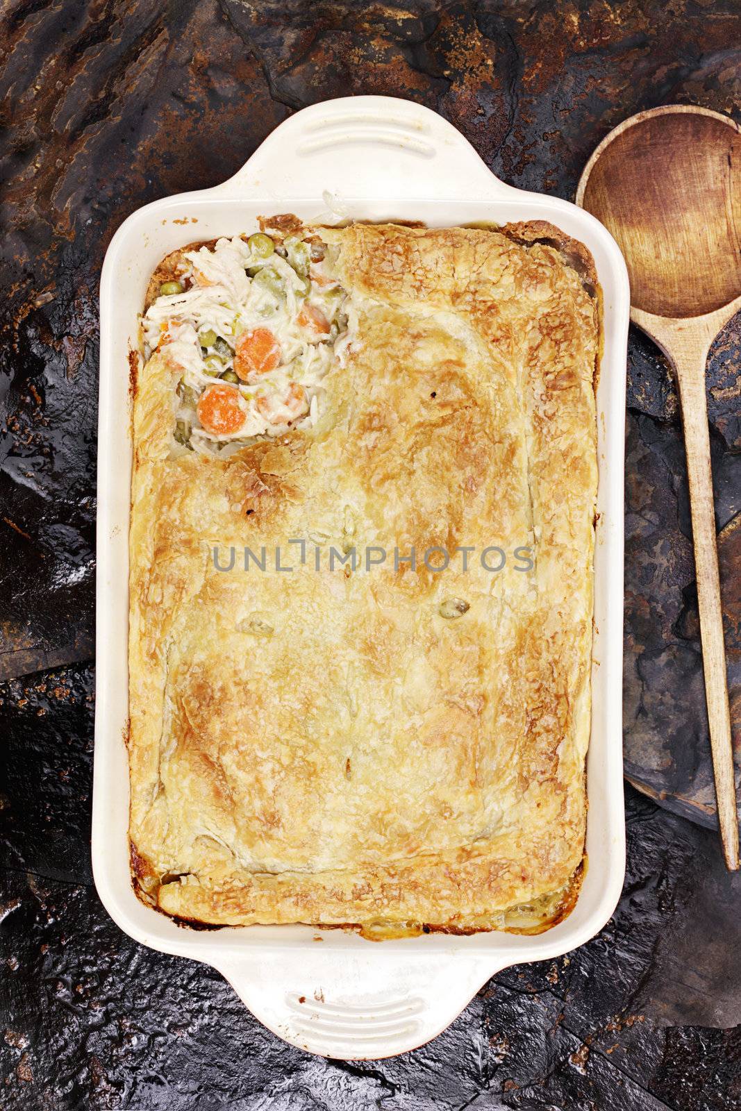 Above view of fresh Chicken Pot Pie with wooden spoon. Section of pot pie removed to reveal chicken, carrots and peas.                    

