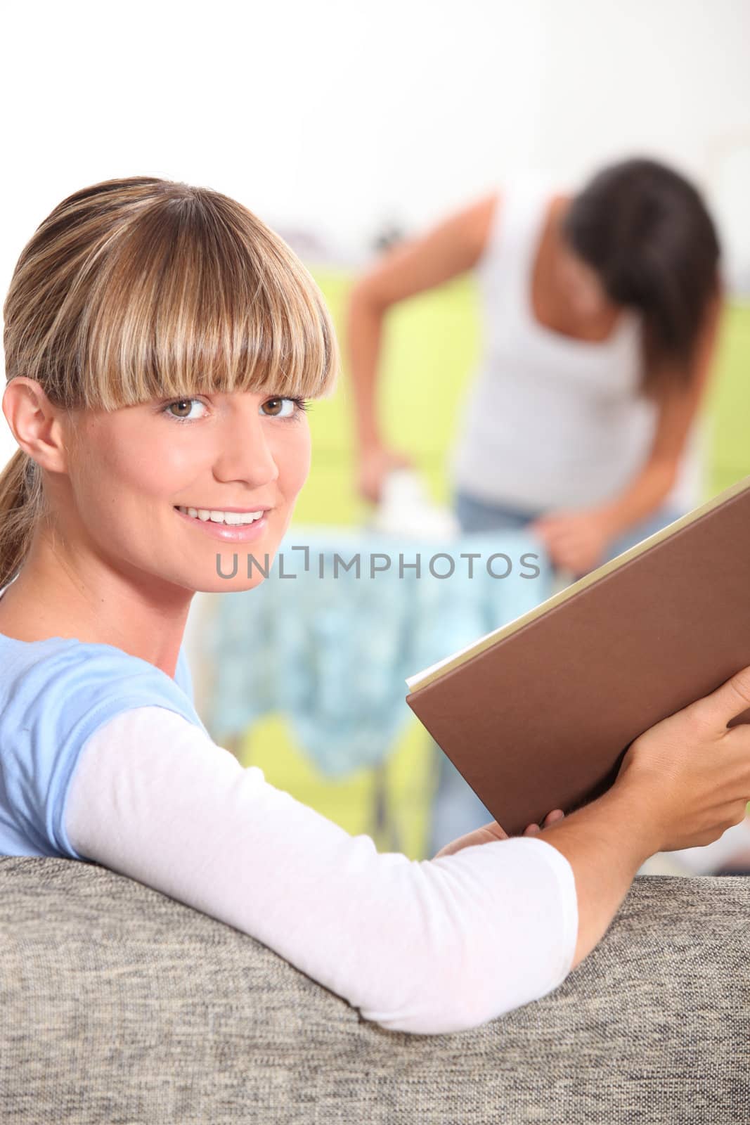 girl reading a book while her mother is ironing by phovoir