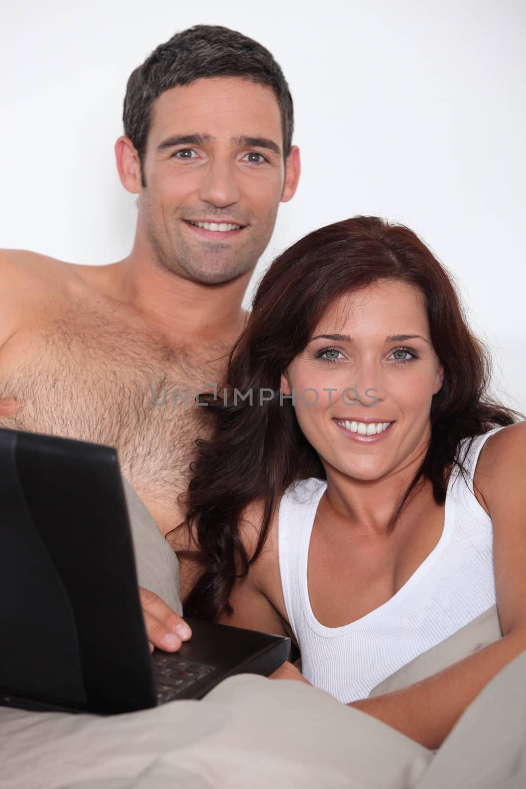 Attractive couple in bed with a laptop by phovoir