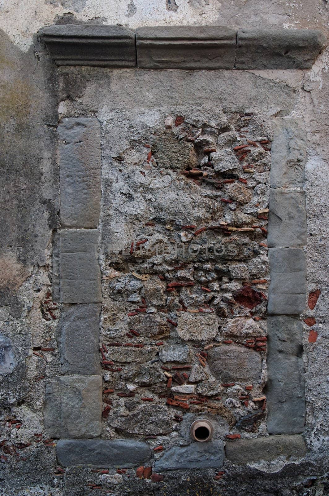 Old window in gray stone wall blocked by bricks and stones