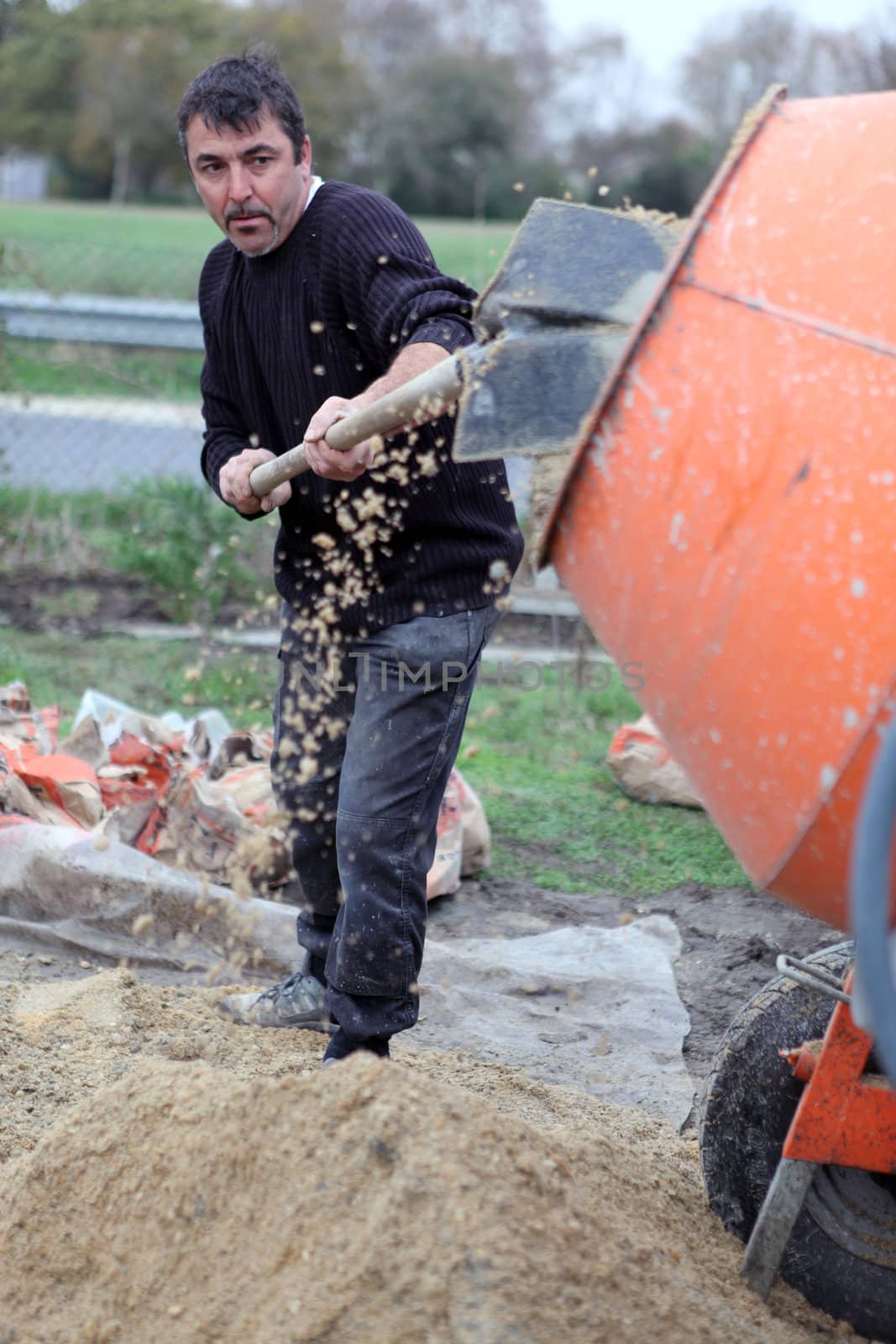 Labourer shovelling gravel into a mixer by phovoir
