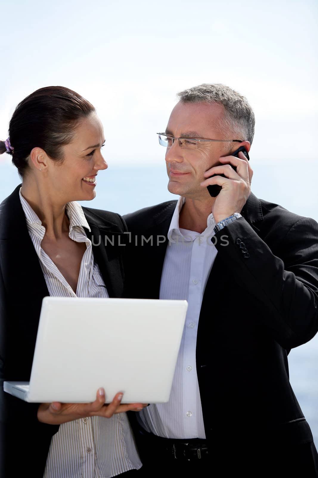 Business couple standing outdoors with a laptop and a phone