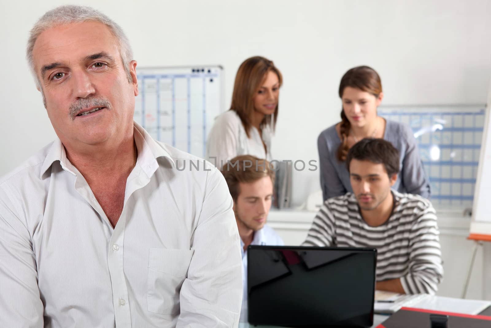 55 years old man watching us and four young people focused on a laptop