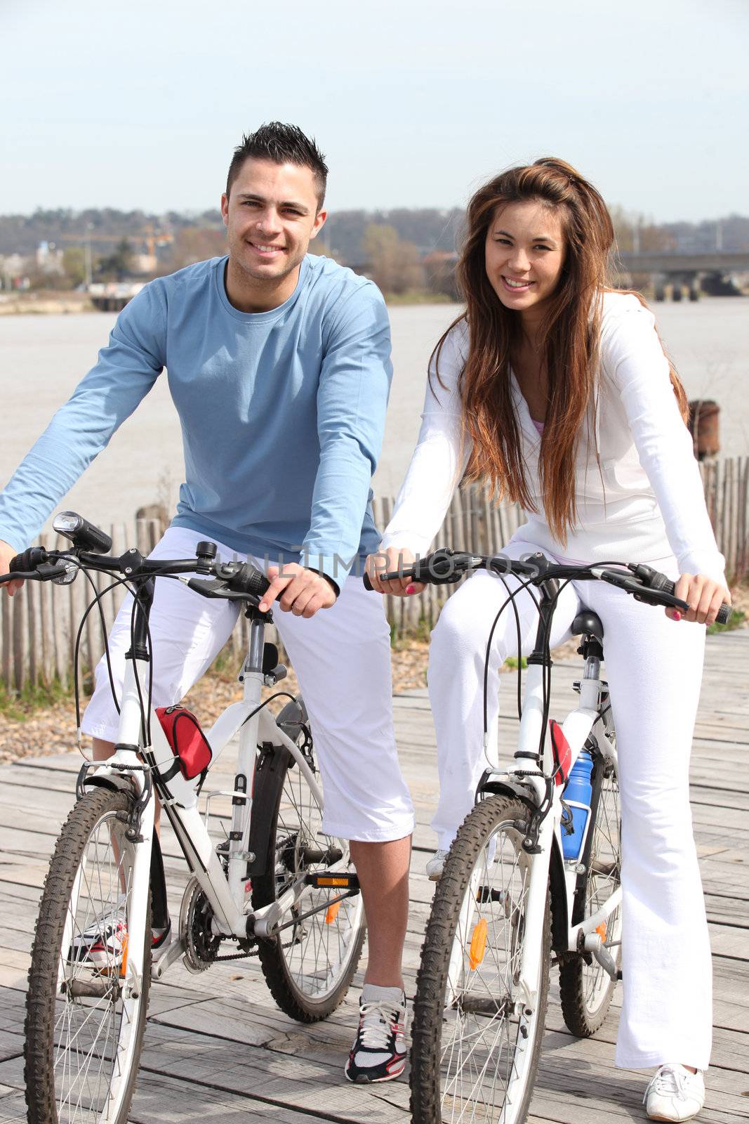 Young couple riding bikes along a river by phovoir