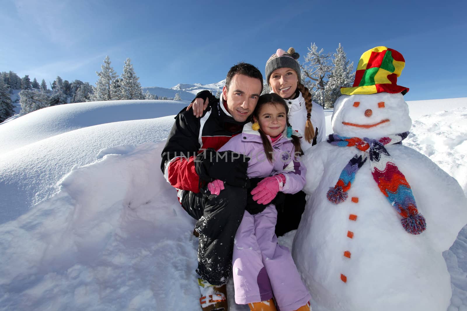 couple posing with child beside snowman at mountain resort by phovoir