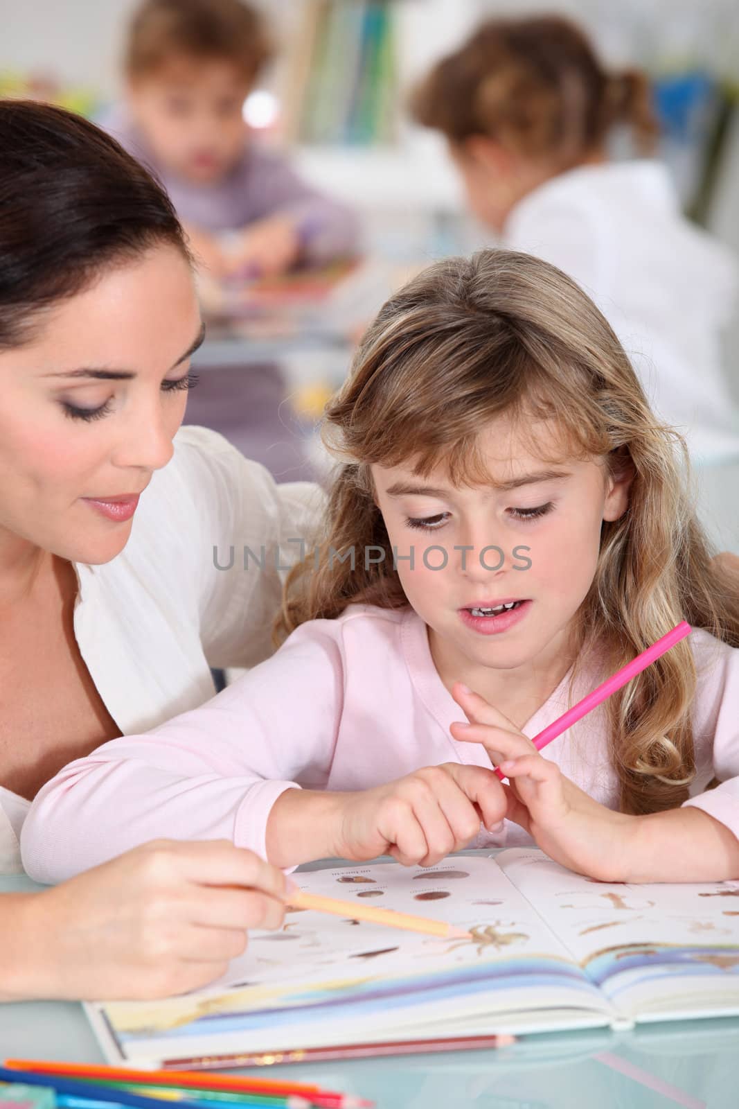 Teacher helping a little girl in the classroom by phovoir