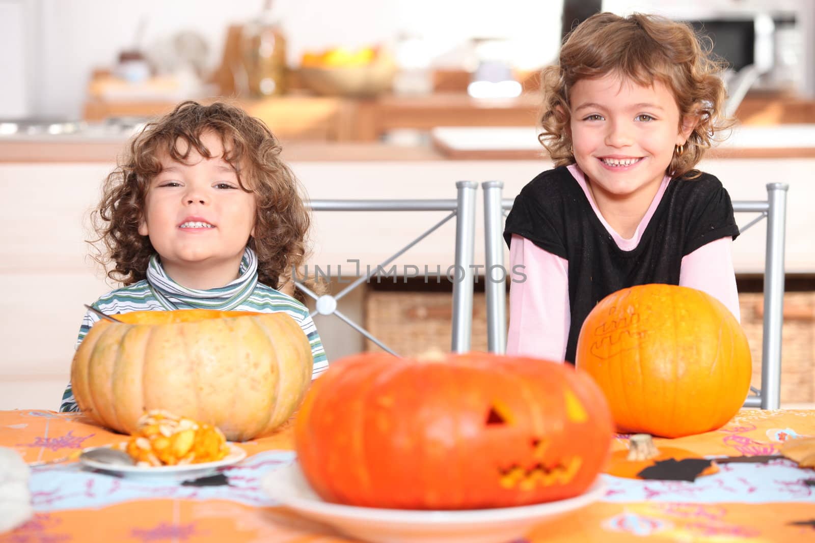 little boy and girl dressed in pajamas posing behind pumpkins by phovoir
