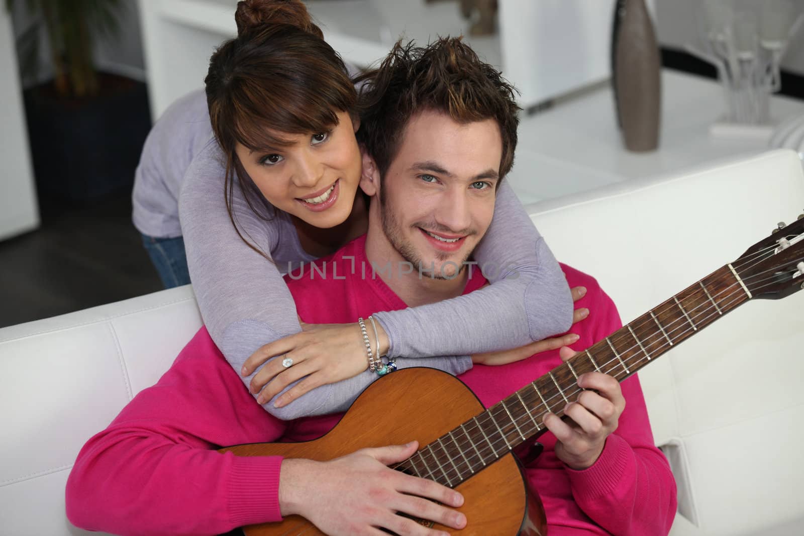 Young couple playing a guitar at home by phovoir