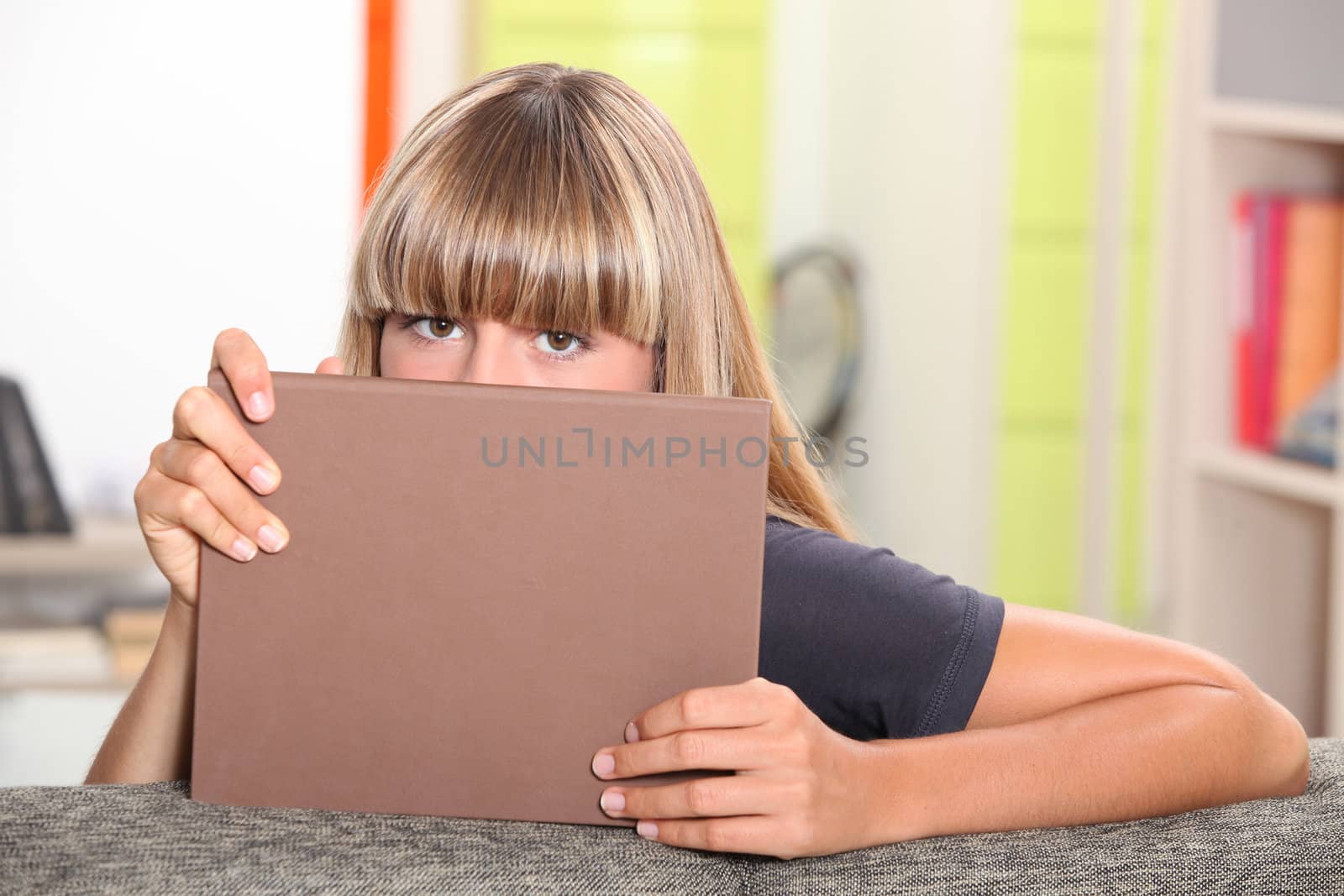 Teenage girl hiding behind a book.