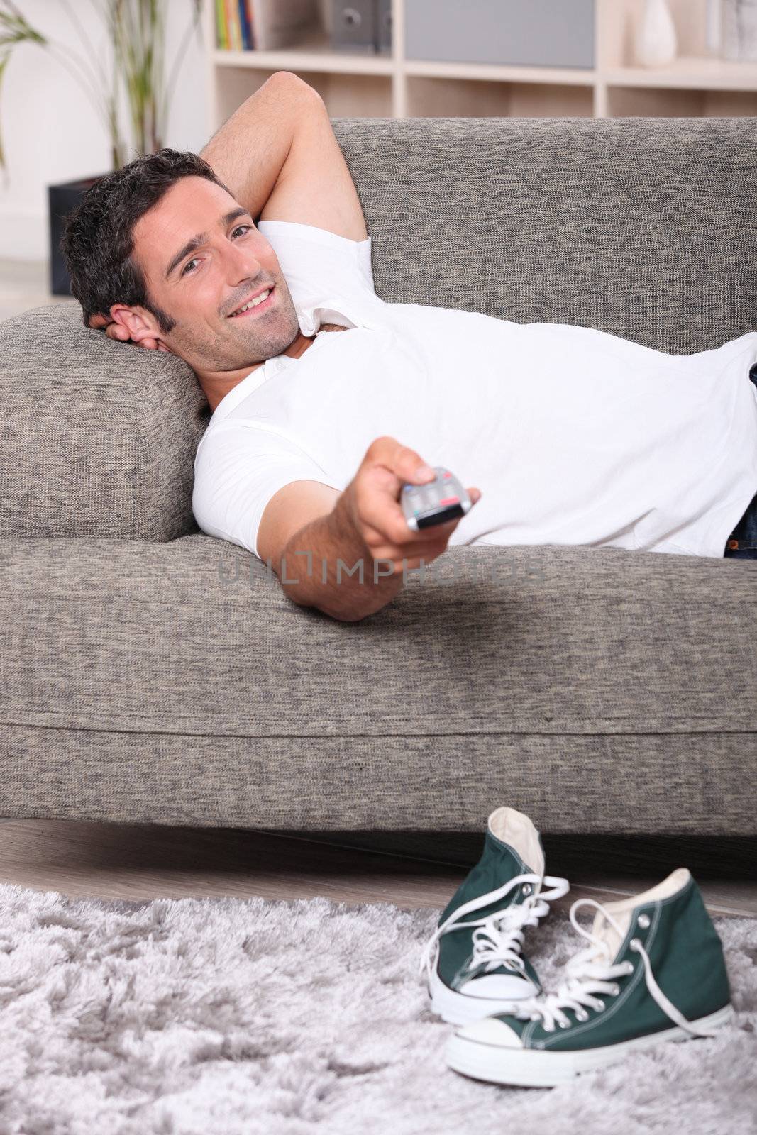 Man lying on couch at home watching television
