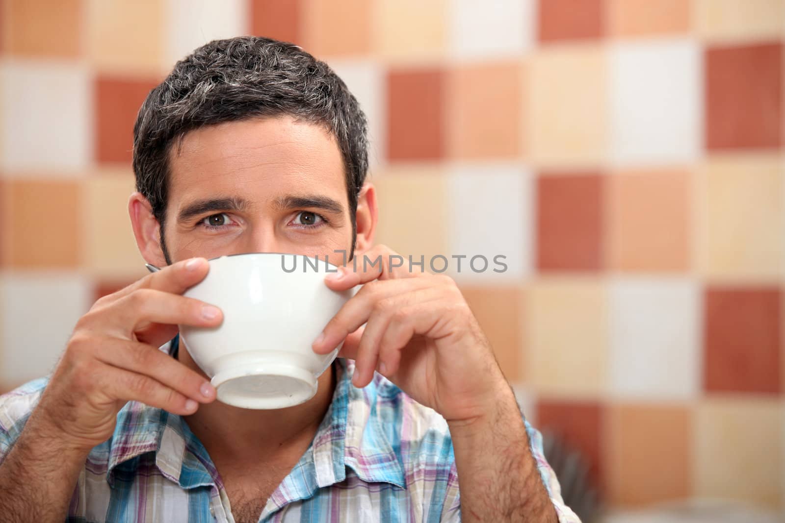 Man drinking from a white bowl in a tiled kitchen