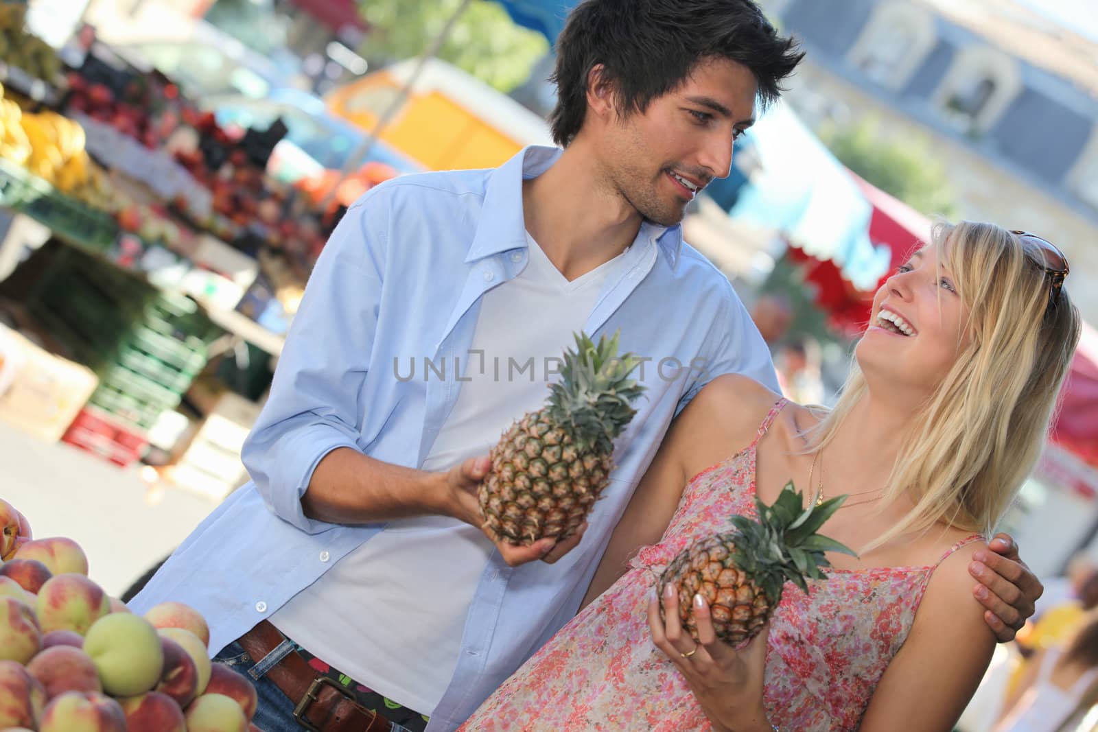 Young couple holding pineapples at a market stall