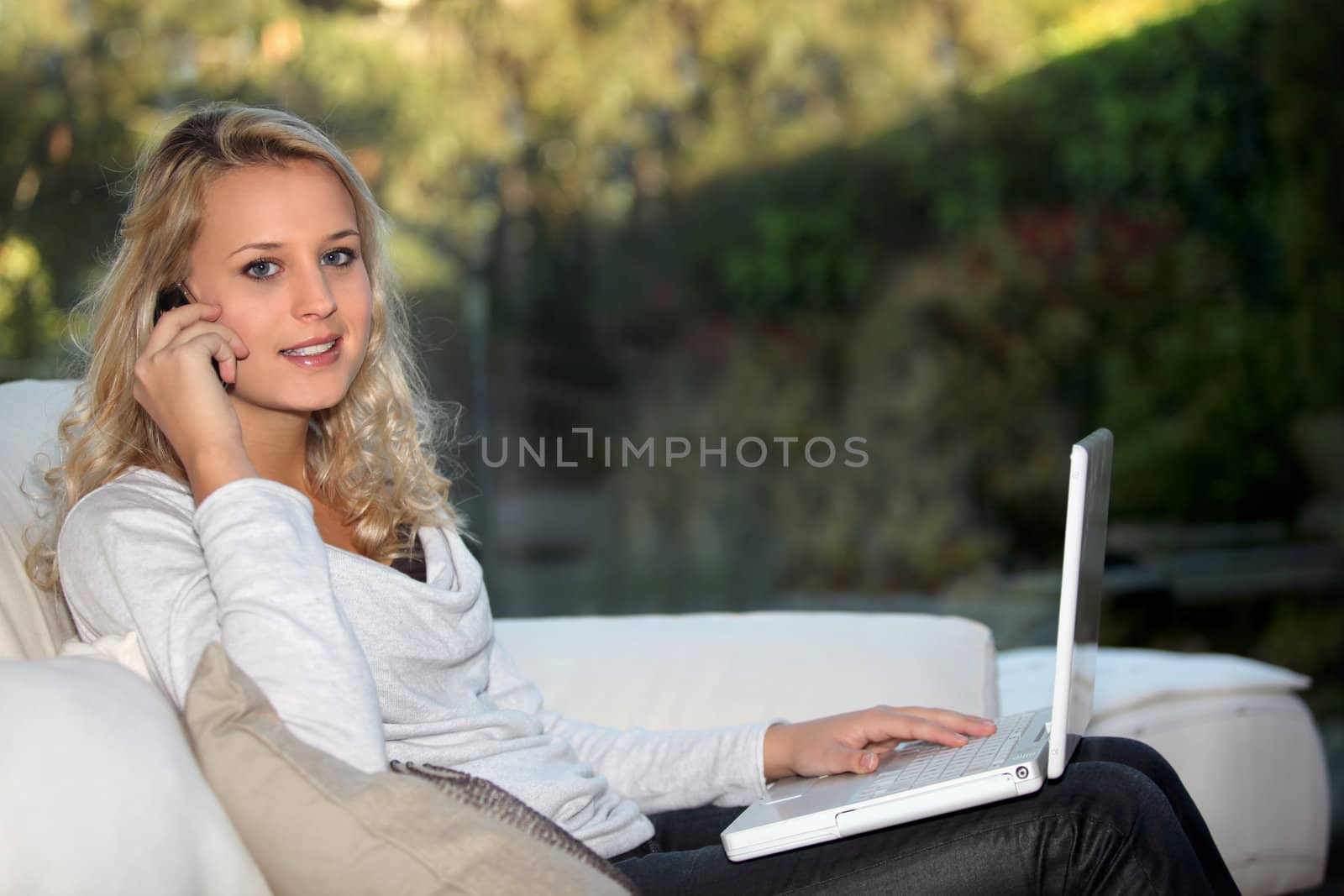 Girl on phone with laptop on a sofa