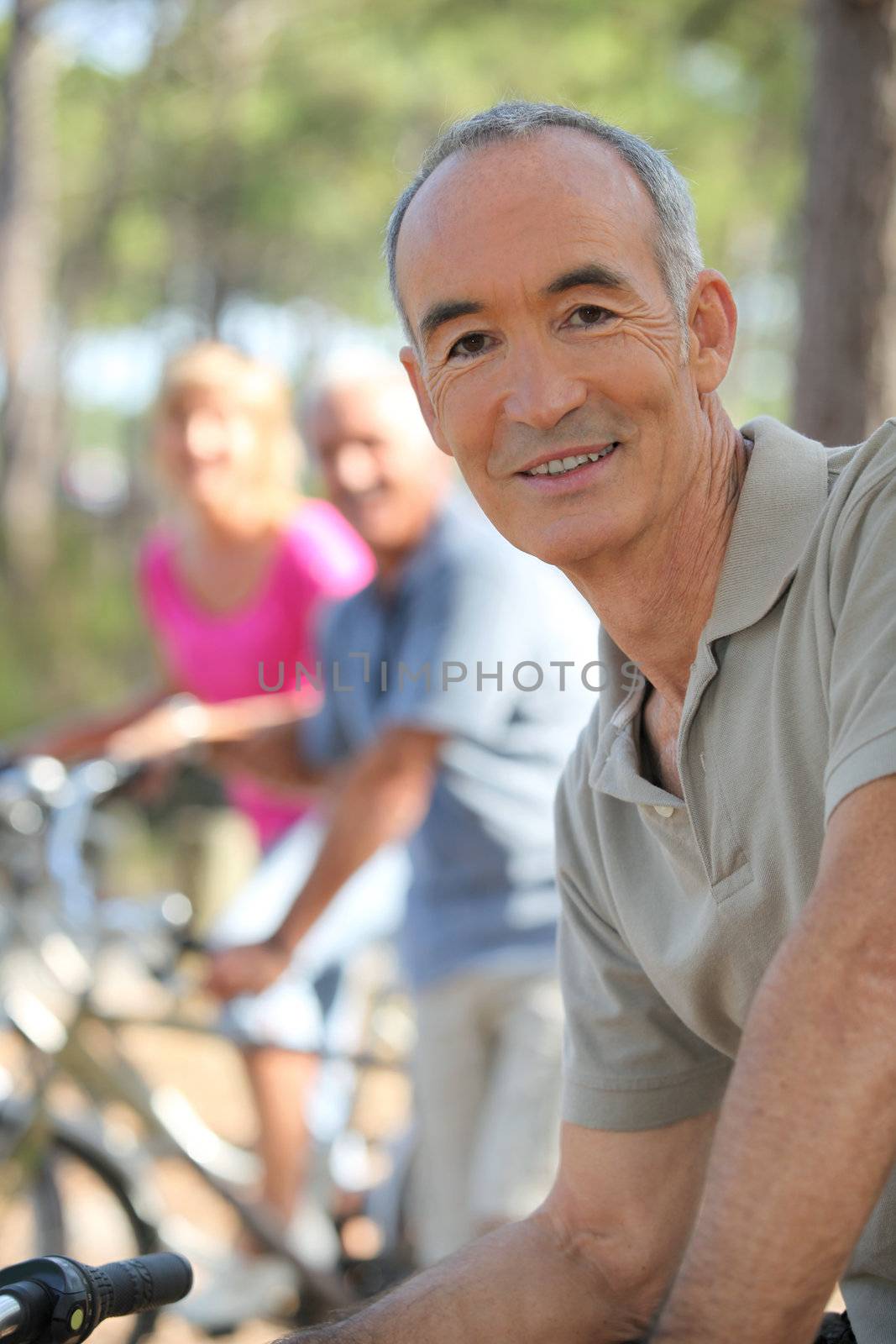 Older man riding a bike in the forest with friends by phovoir