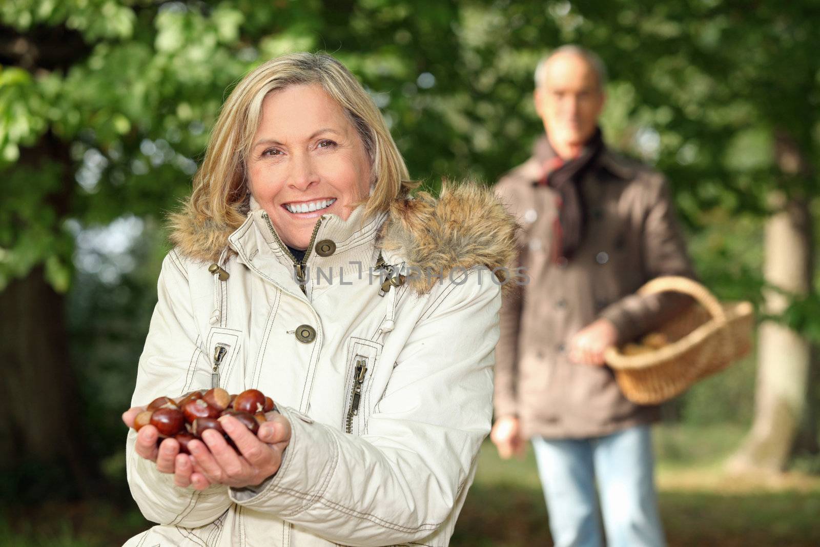 mature woman in woods with husband showing chestnuts by phovoir