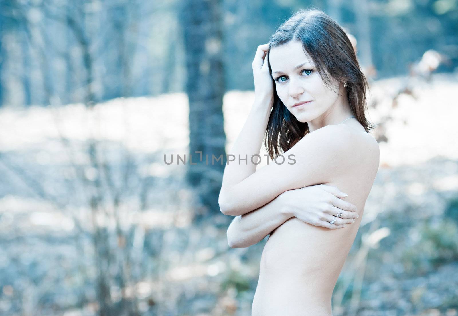 Topless young woman hiding her naked chests under her arms
 in a forest.