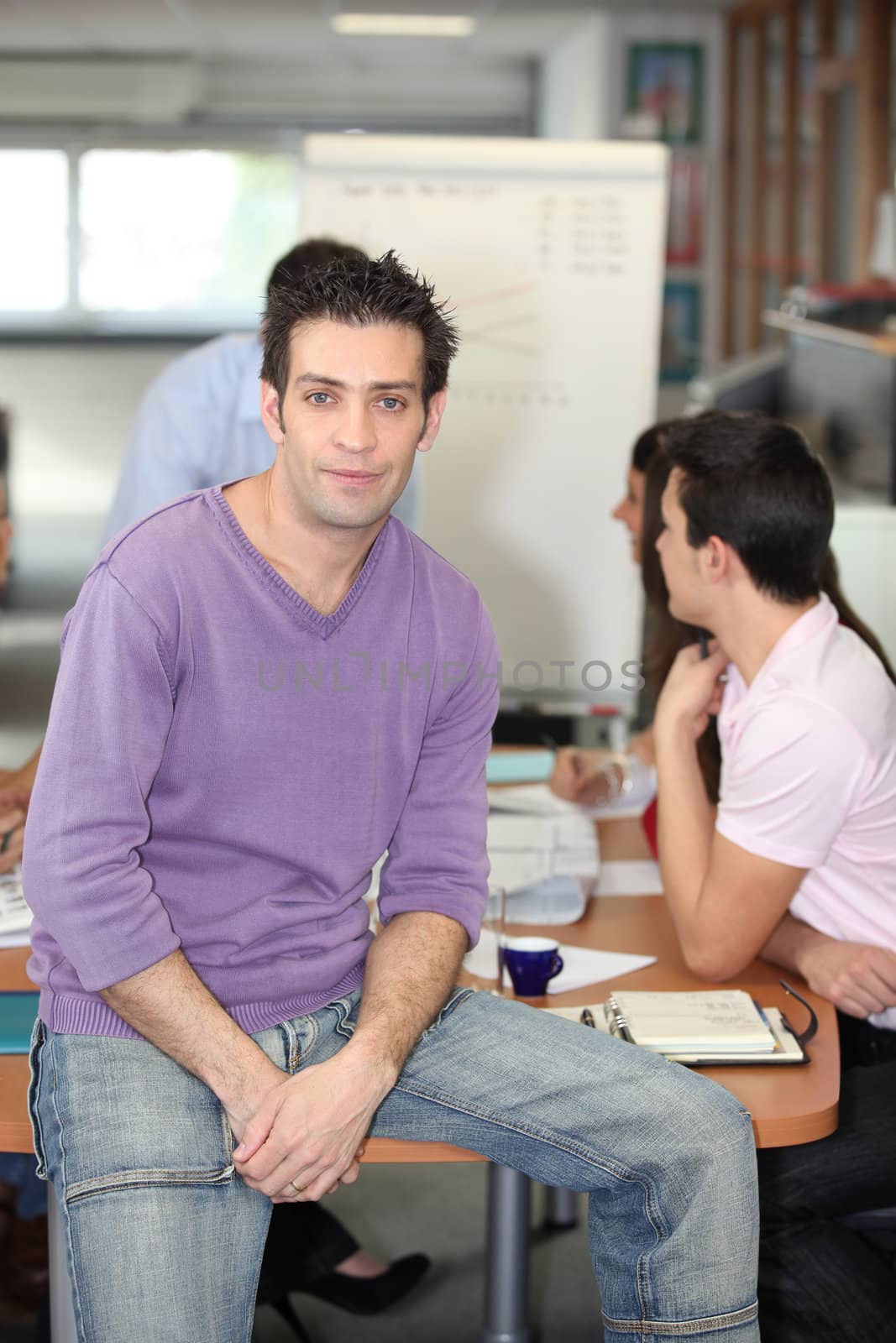 Man in jeans perching on an office desk by phovoir